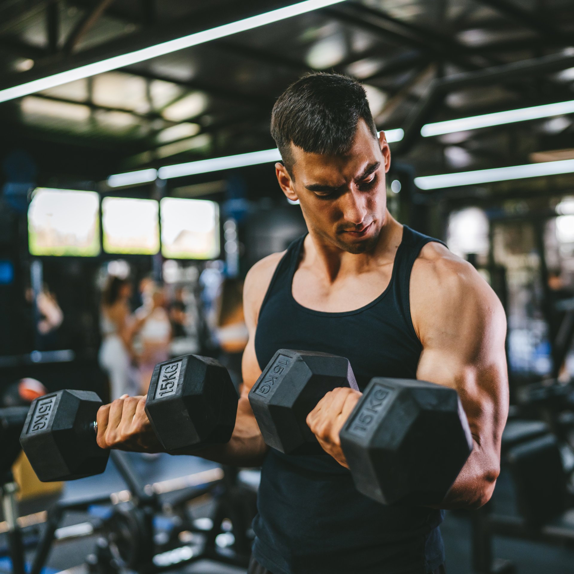 young muscular sports man do biceps workouts with dumbbells in gym