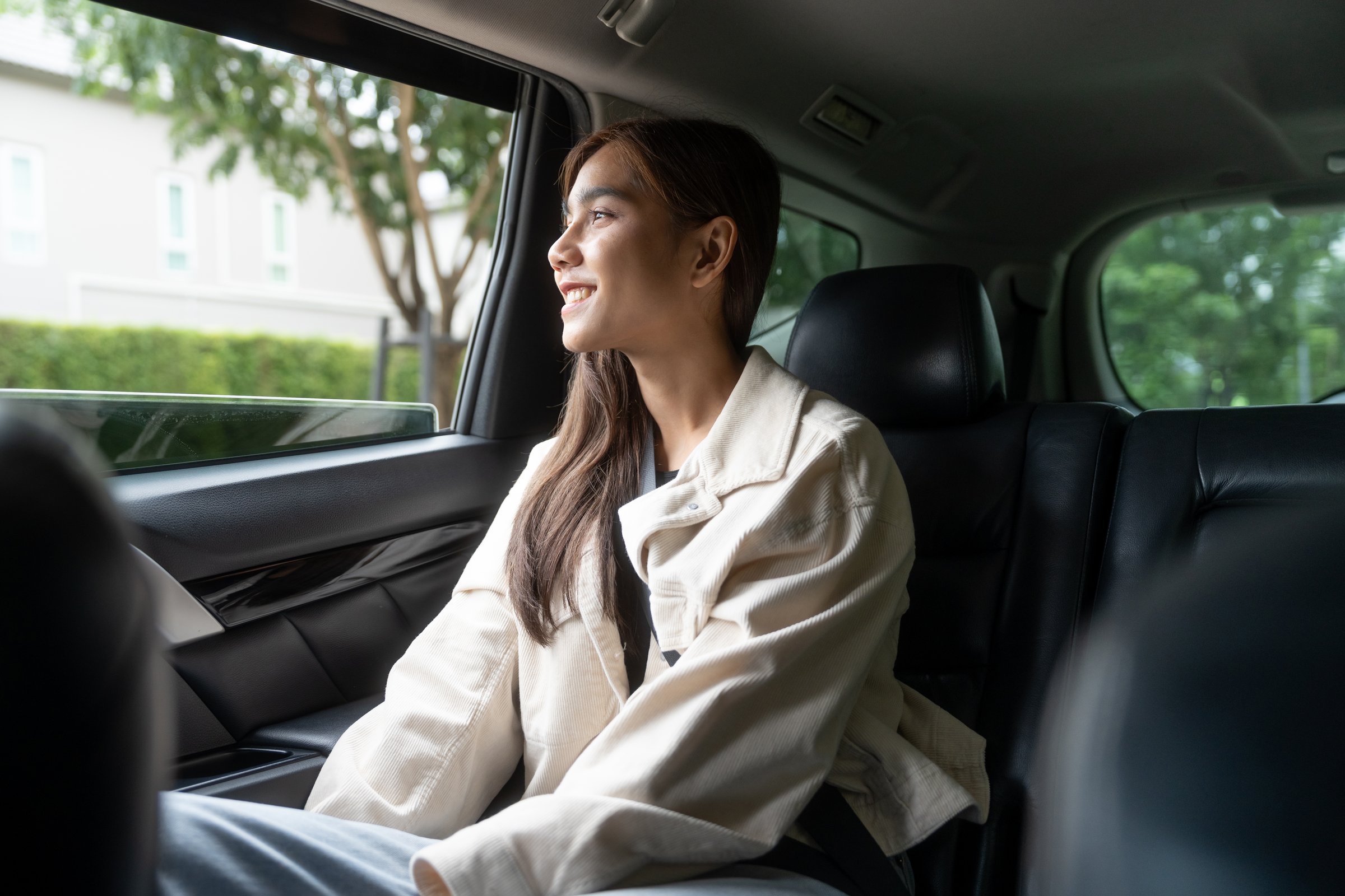 Relaxing moment of beautiful woman sitting in car back seats with safety belt and look out in the window. Female happy in car while traveling on the road to your destination.