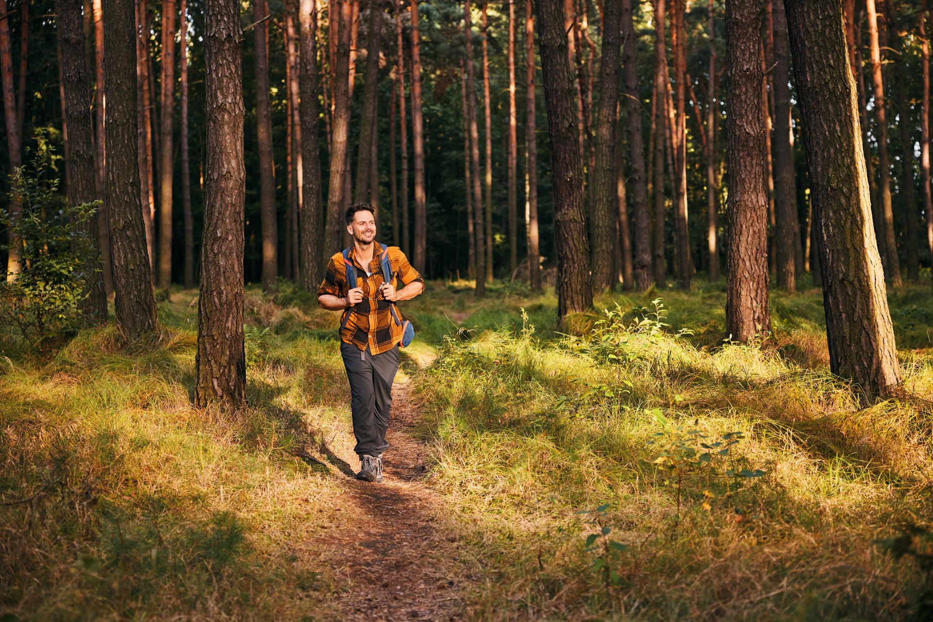 Man walking through the forest with backpack during sunny autumn afternoon