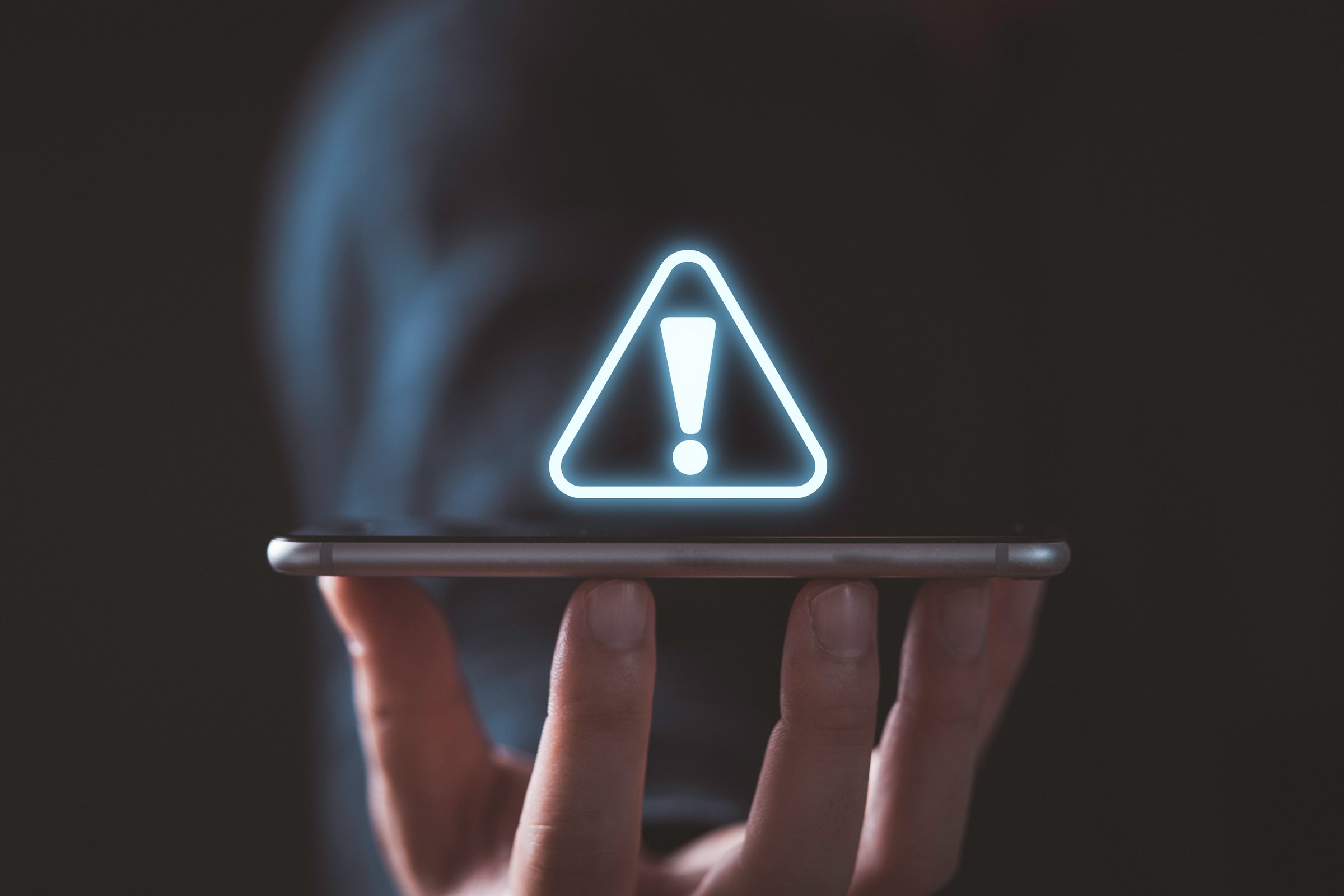 Businessman holding smartphone with triangle caution warning sign for notification error and maintenance concept.
