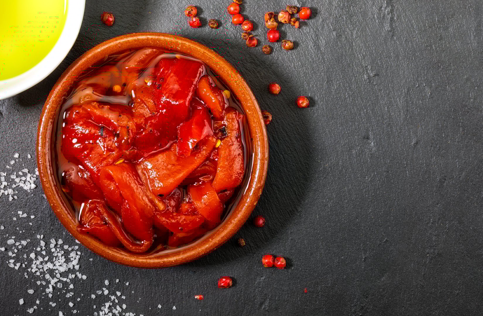 Delicious and appetizing red peppers roasted at home. Extra virgin olive oil, salt and pepper. On textured background in black.