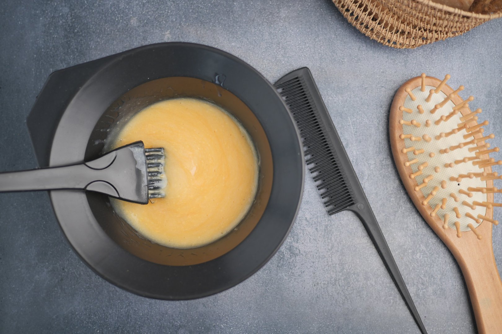 Mixing a vibrant hair dye color with tools on a grey countertop.
