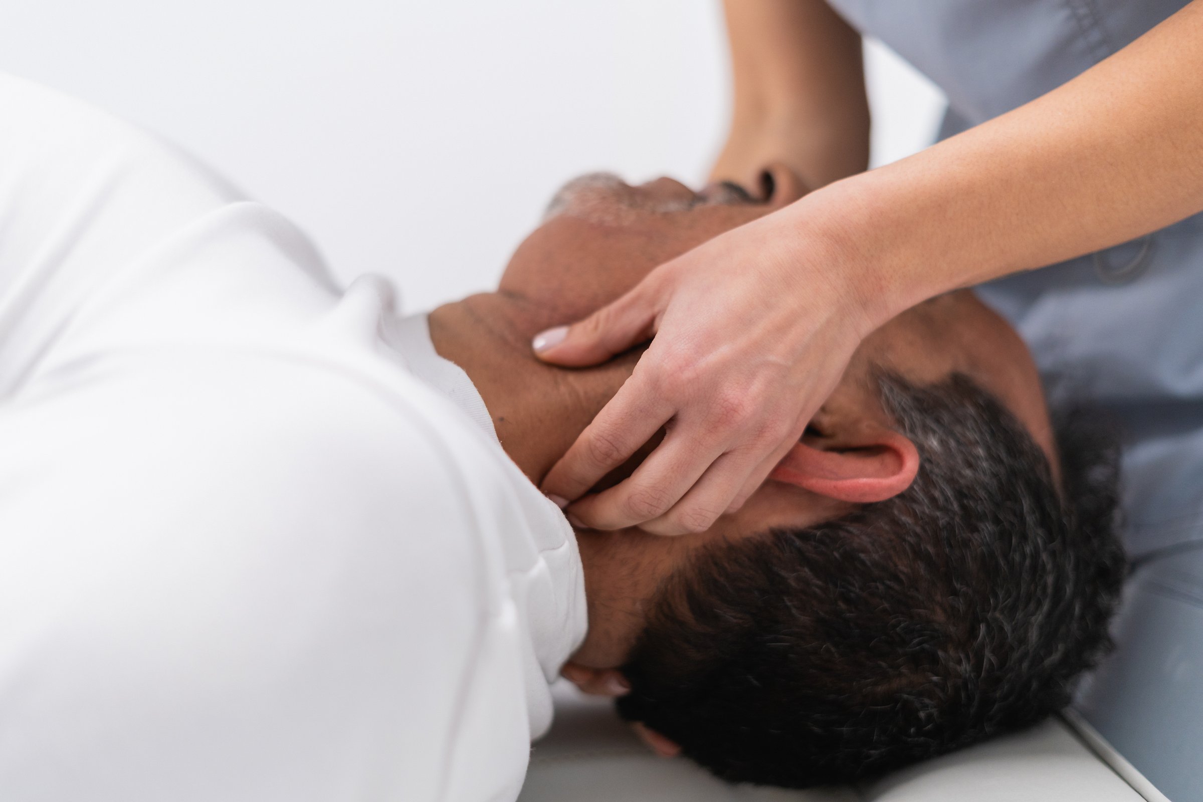 Physiotherapist performing neck massage on mature male patient to alleviate pain and improve mobility