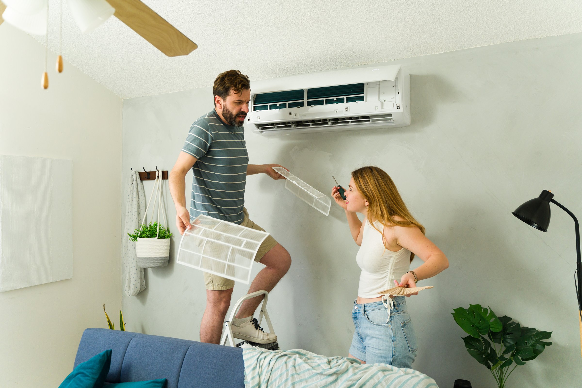 Homeowners cleaning and replacing dirty air filter in a wall mounted mini split air conditioning unit in bedroom during summer