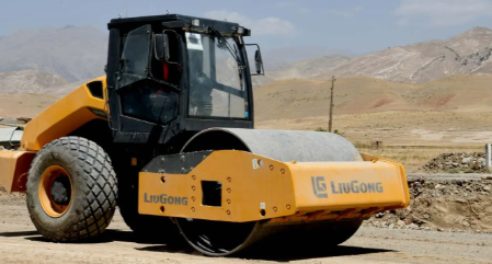 A Liugong road roller working on a dirt road with mountains in the background on a clear day.