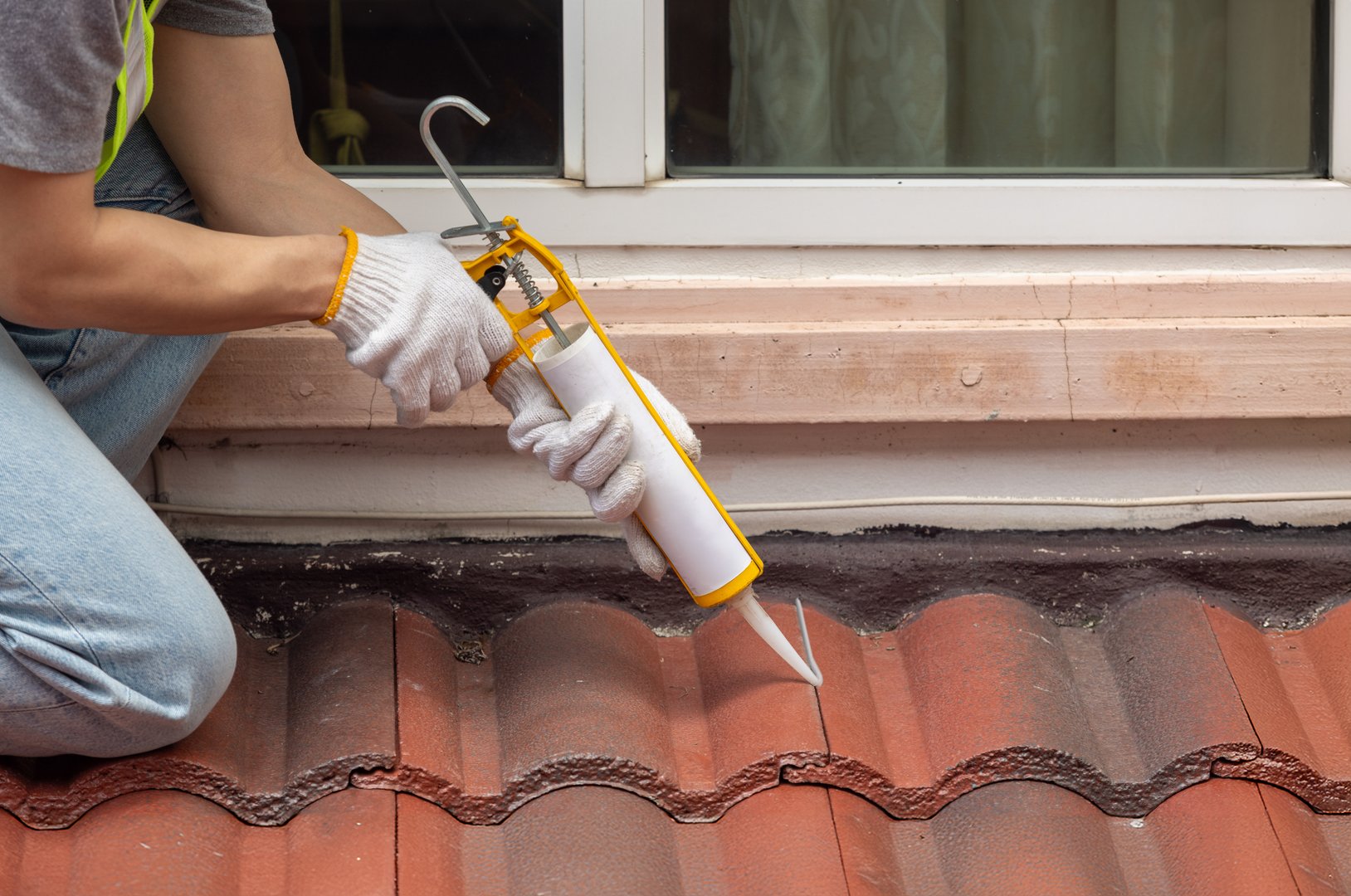 Construction worker using silicone sealant adhesive to fix crack of the old tile roof.
