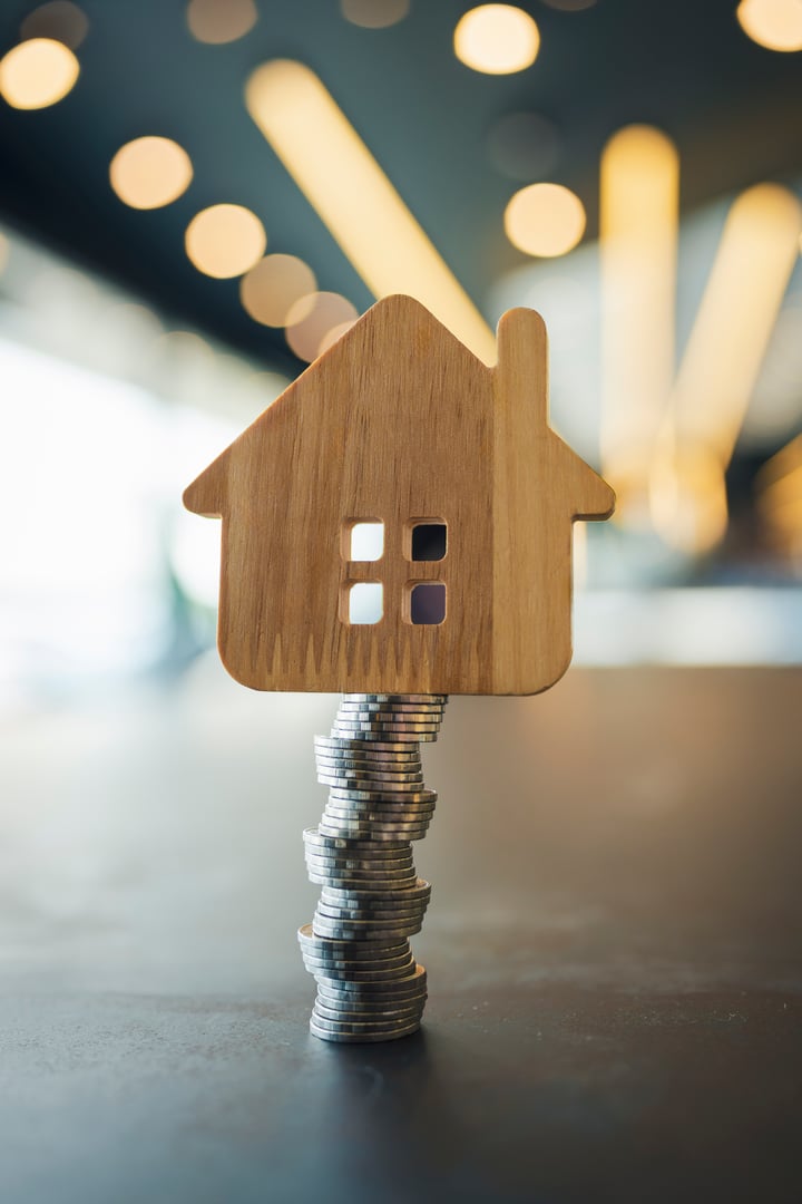 A model of a wooden house and coins placed in a stack, staggered in order to make it prone to falling. The concept of risk in real estate investment that is related to the value of money.