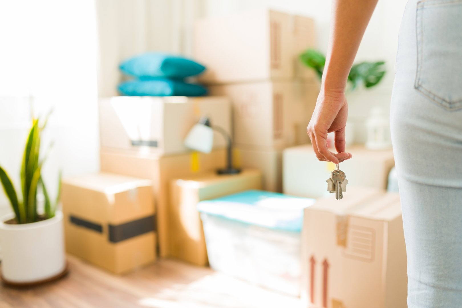 New homeowner: young woman holding keys in living room surrounded by cardboard boxes, representing the concept of moving