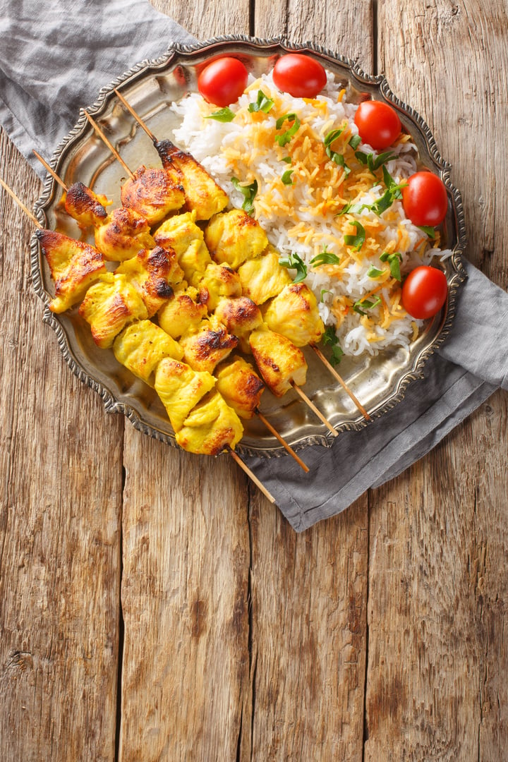 Grilled chicken kebab is known as jujeh kabab with rice closeup on the plate on the table. Vertical top view from above
