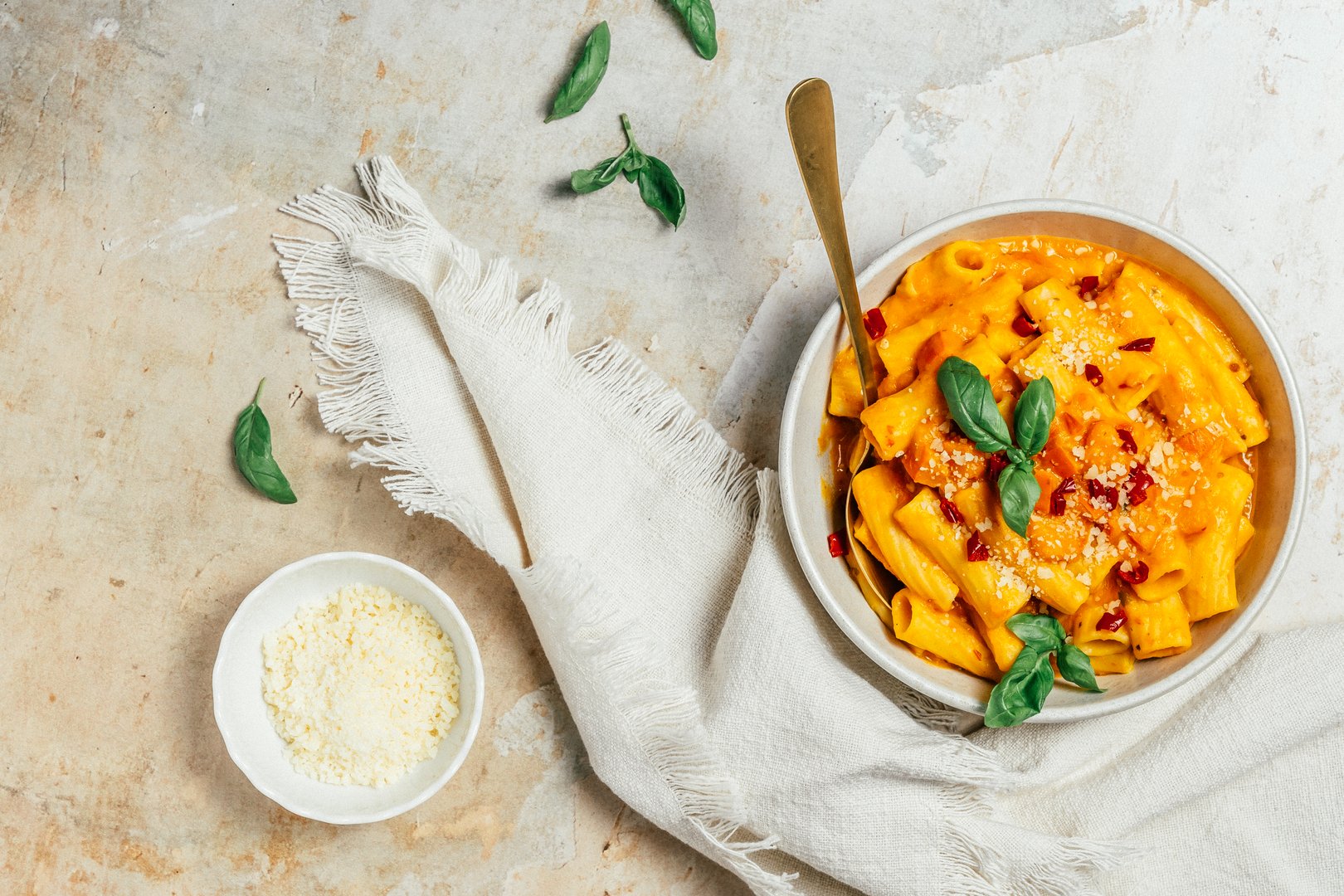 Italian rigatoni pasta with creamy pumpkin sauce, fresh spring onions and parmesan cheese, pumpkin noodle bowl, top view