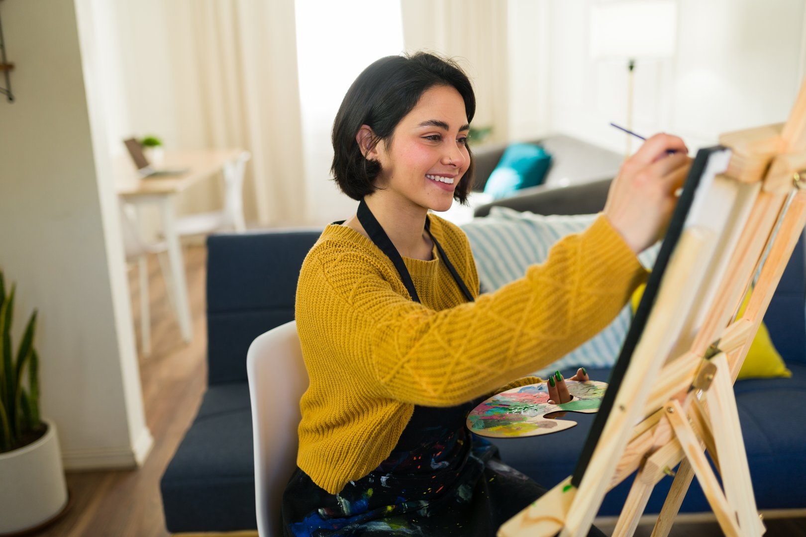 Happy young woman painting on canvas with oil paint and brush working from home in her art studio