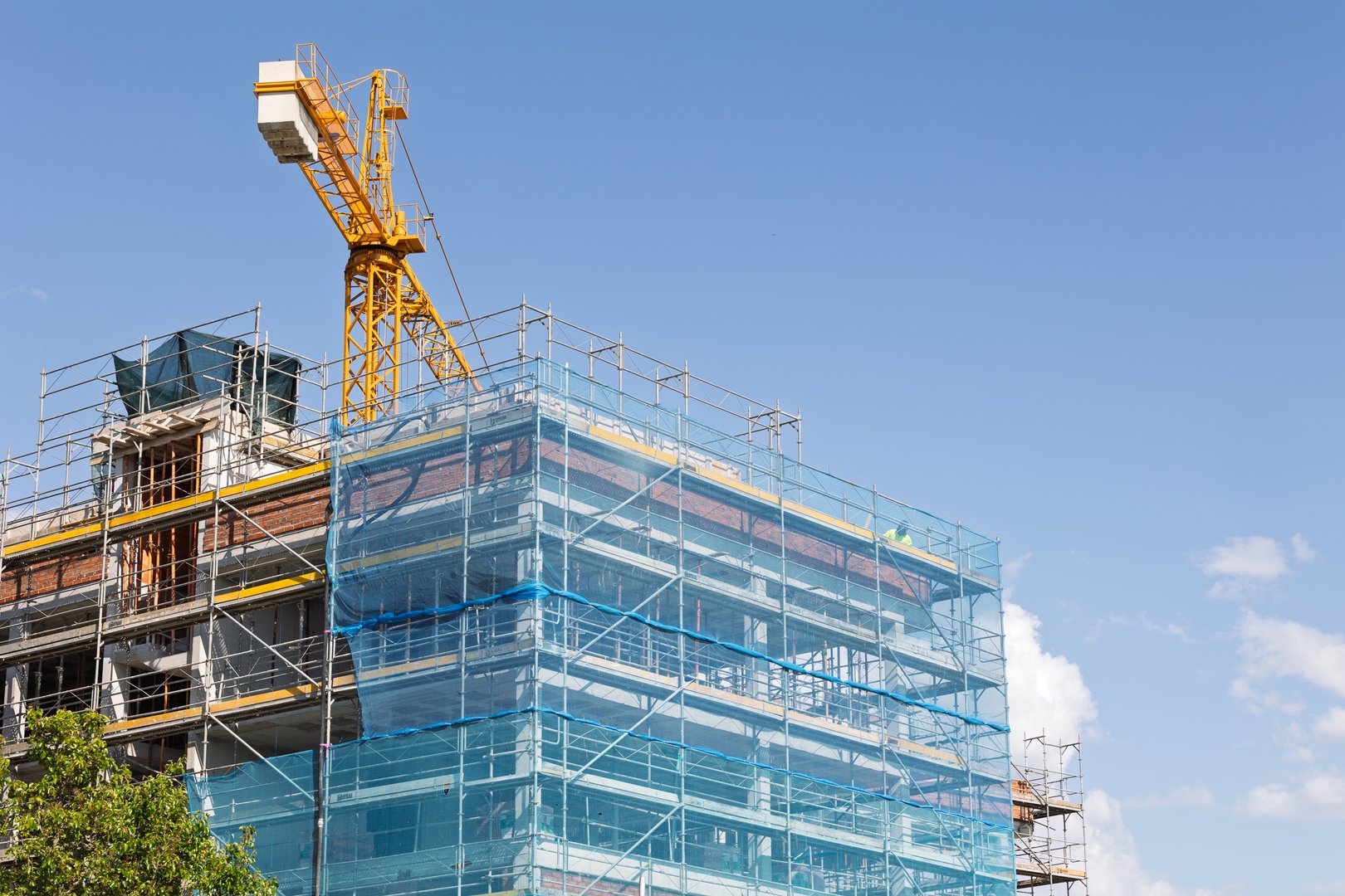 Construction crane building a modern edifice with scaffolding and blue safety net