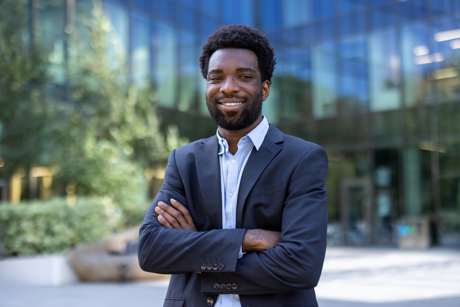 Portrait of successful confident businessman. Man in business suit smiling and looking at camera. African American company employee outside office building with arms crossed.