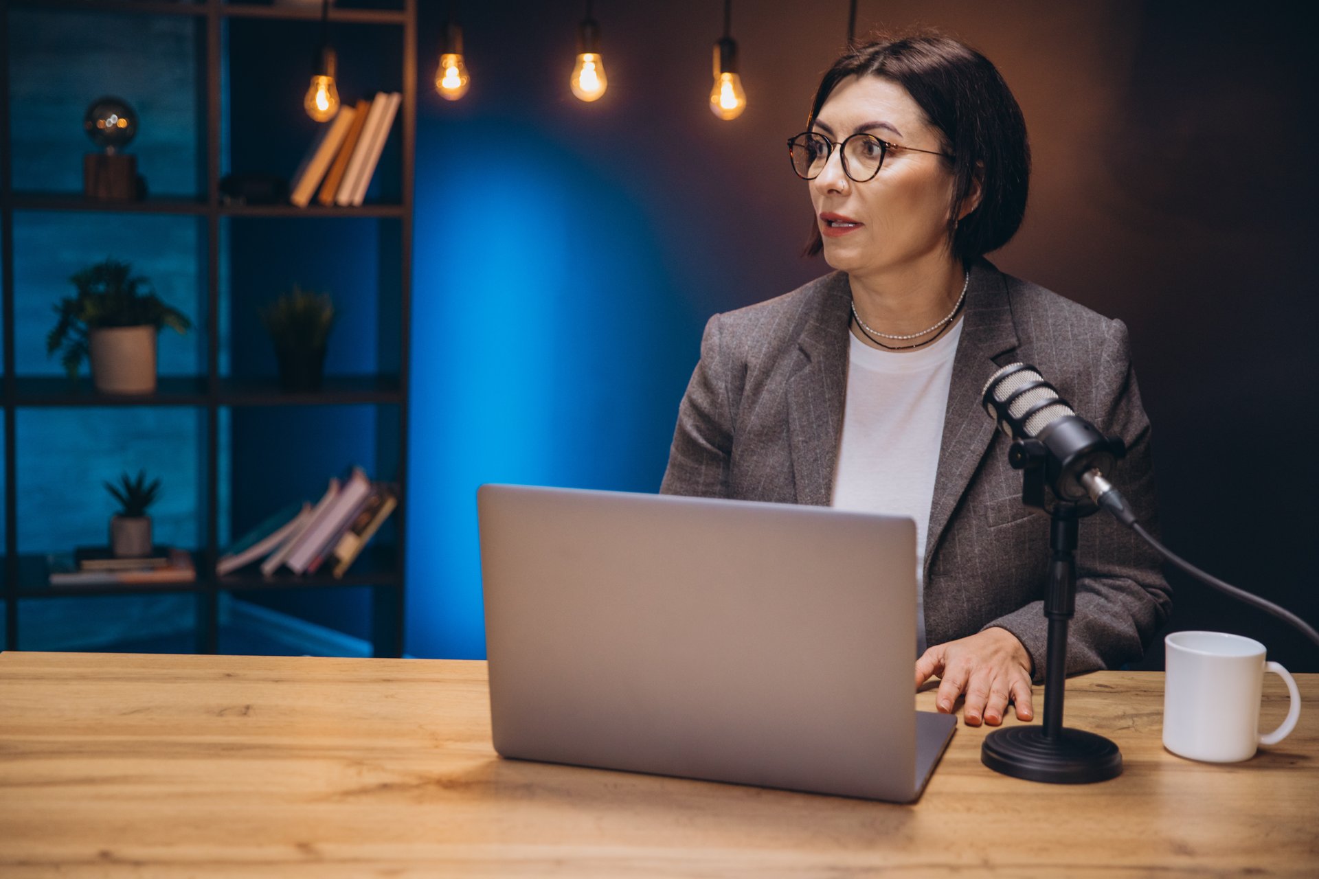 Mature female radio professional recording podcast, speaking into microphone within broadcasting studio
