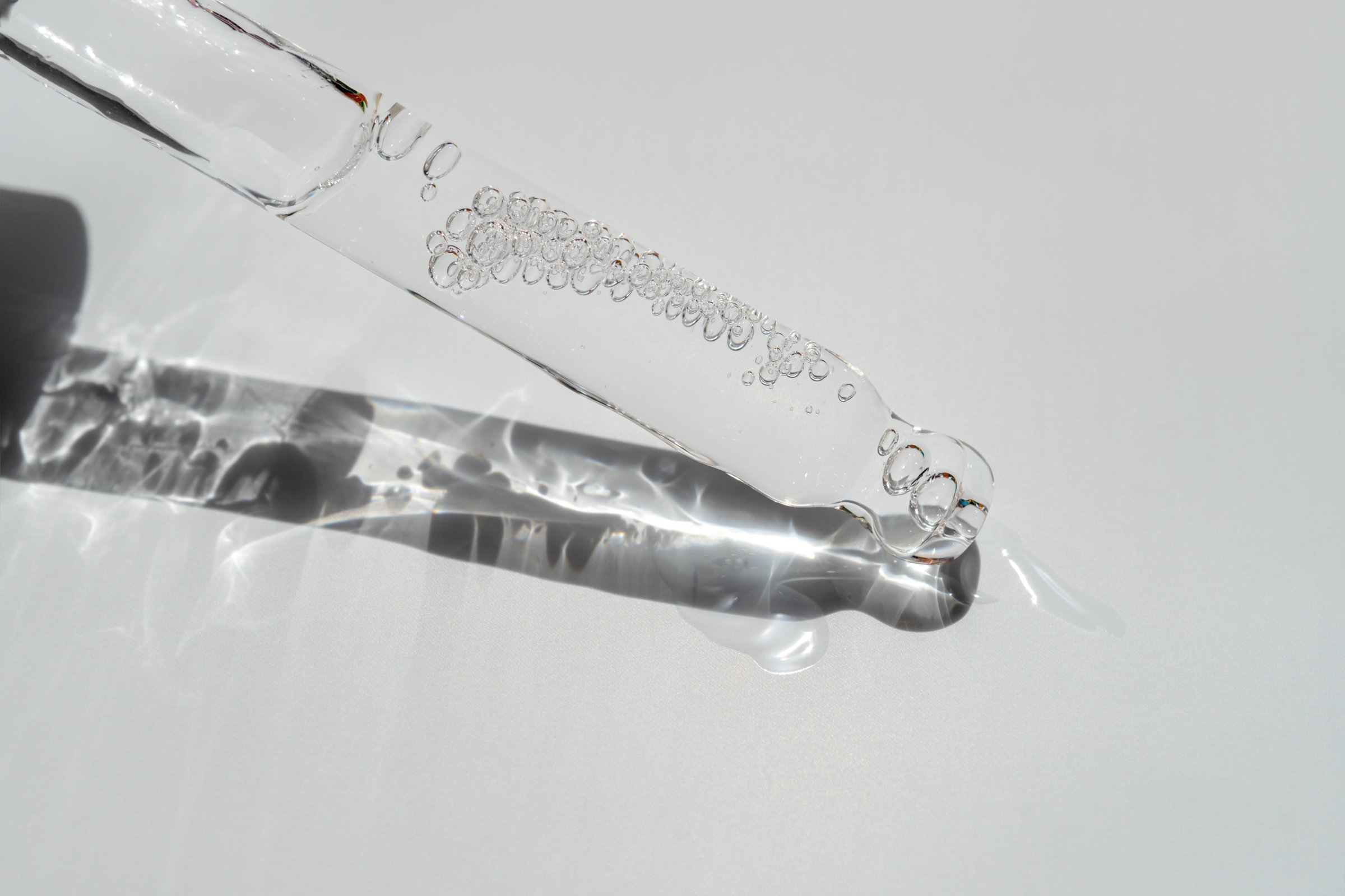 Glass pipette with facial serum on a light background. Essential oil close-up in a pipette. A skin care product with hyaluronic acid in a pipette.