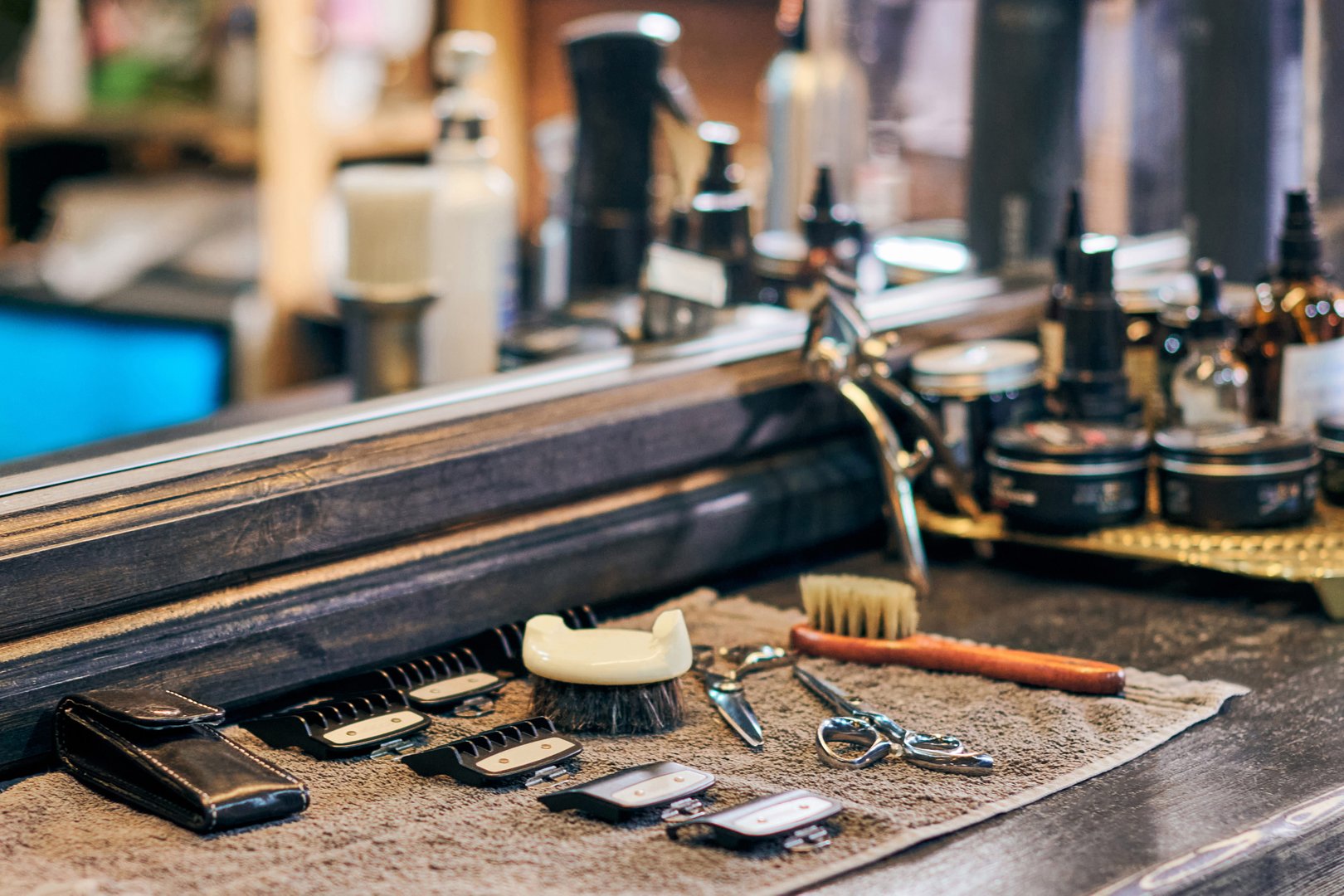 Barbershop haircut tools barber equipment on wooden countertop front of mirror, old vintage style interior. Hairdresser tools for stylish hair cut, clipper guide combs, scissors and hairbrushes