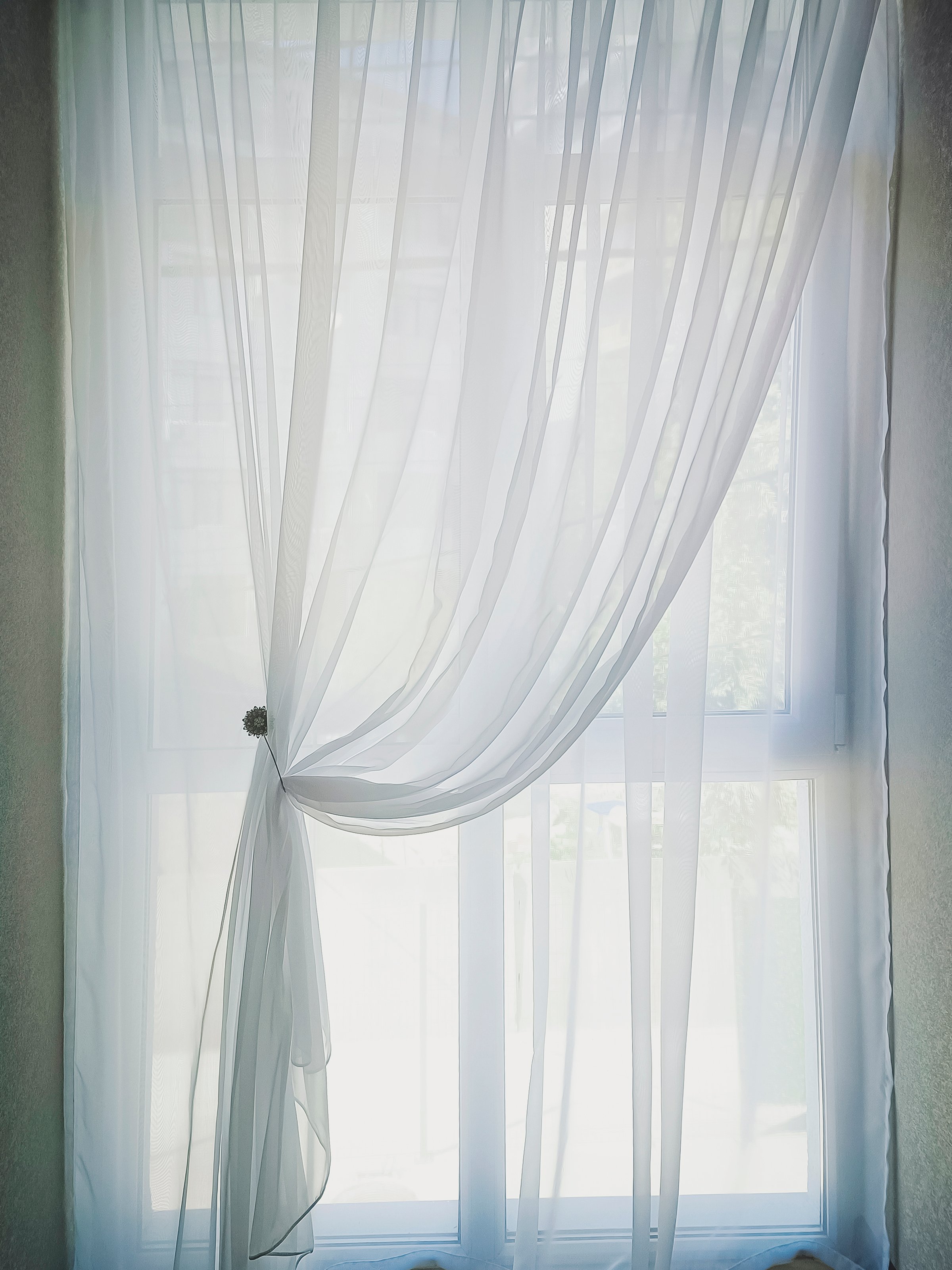 White transparent tulle curtains hang on the window. Close-up, vertical photo.