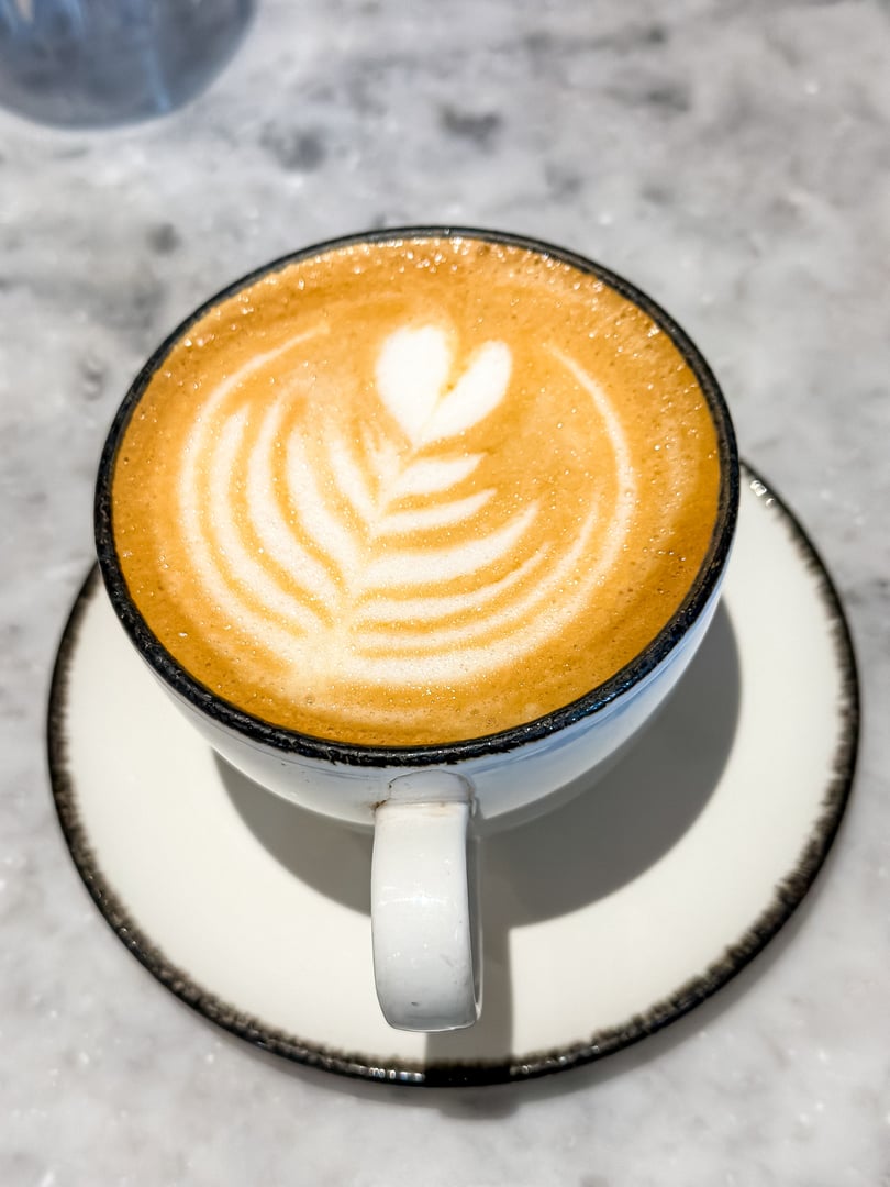 A mug of flat white coffee on a marble background. Coffee art. Heart flower shape latte art. Copy space