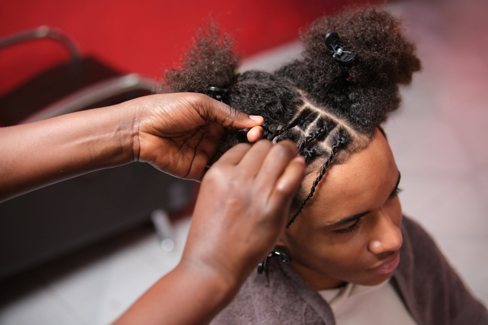 Top-down view of afro man getting hair braided in salon