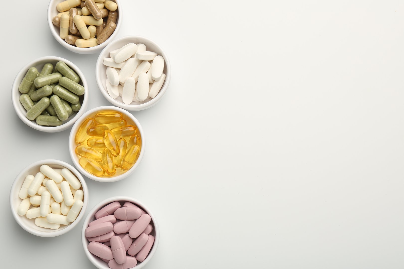 Different vitamin capsules in bowls on white background, flat lay. Space for text