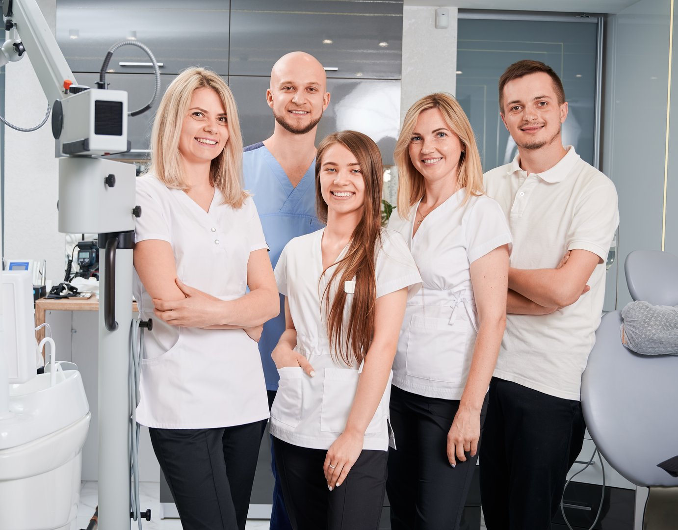 Dentists looking at camera and smiling while posing in modern dental office. Women expressing positive emotions while standing beside joyful male colleagues. Concept of dentistry and dental staff.