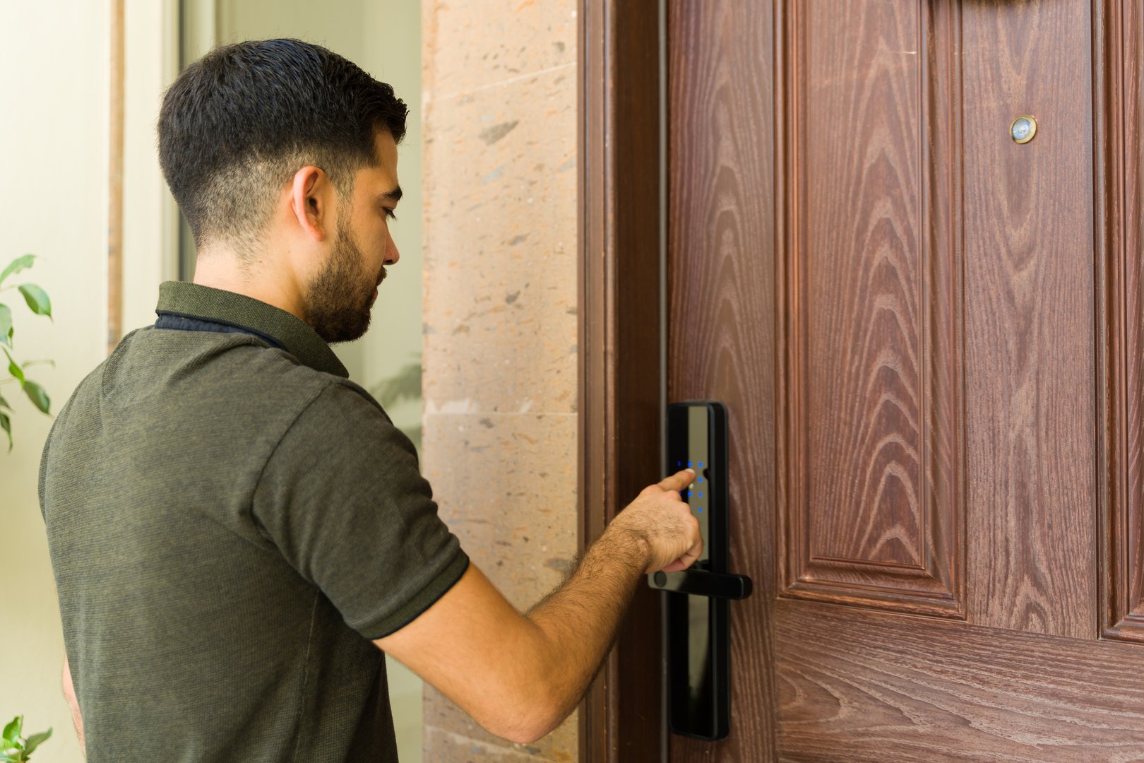 Hispanic man in front of a smart lock on a door, using a digital touchscreen keypad to enter his house