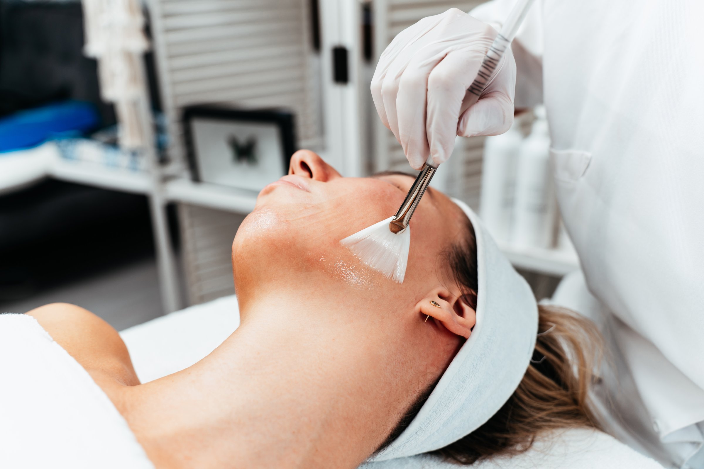 Professional beautician applying glycolic acid peel on face of beautiful young woman