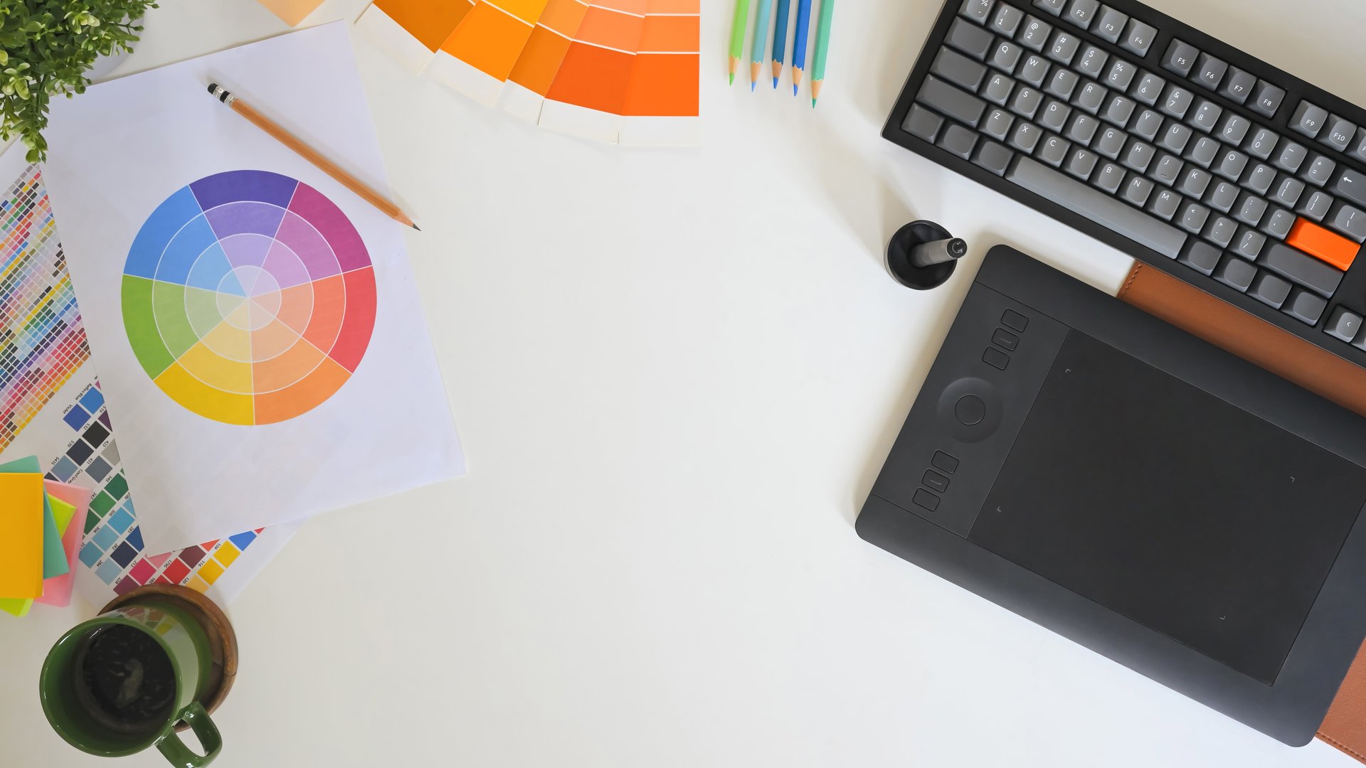 Top view of creative workspace with color palette, digital tablet, and notebook sketching logo design on clean white desk.