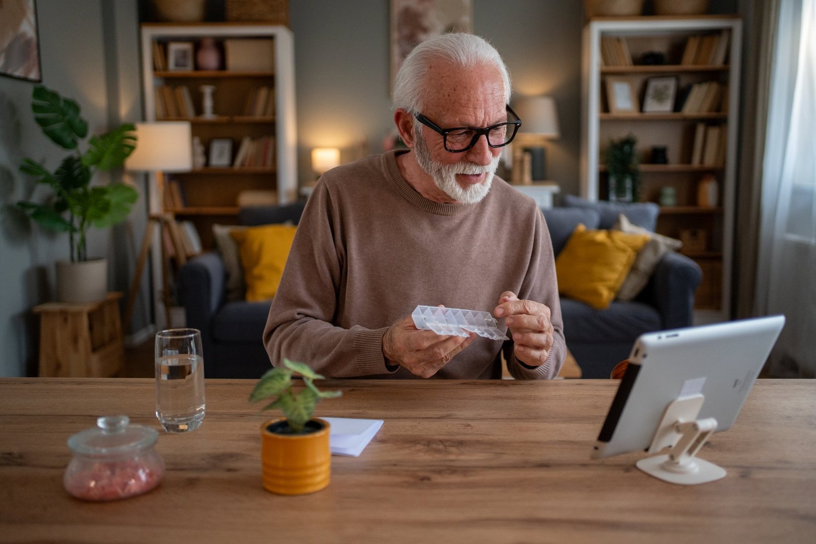 Senior man sitting comfortably at home, engaging in an online medical consultation, showcasing his daily pill organizer to the doctor during a video call for personalized healthcare advice