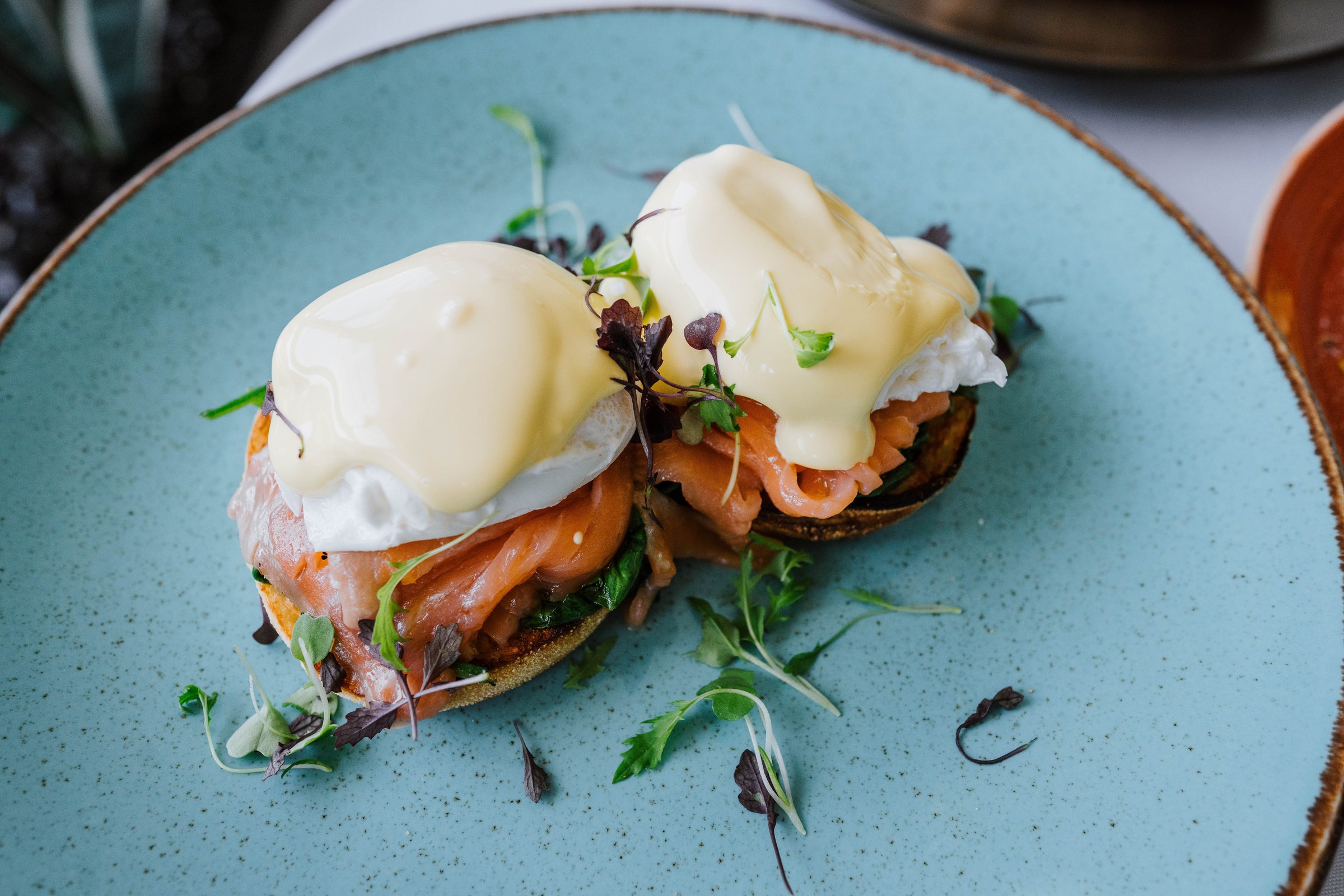 Delicious eggs benedict with smoked salmon and hollandaise sauce on a blue plate, garnished with microgreens.