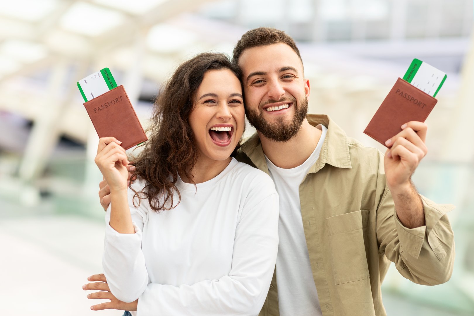 Happy Young Man and Woman Holding Up Passports In Airport And Smiling At Camera, Excited For Upcoming Trip, Loving Couple Enjoying Travelling Together