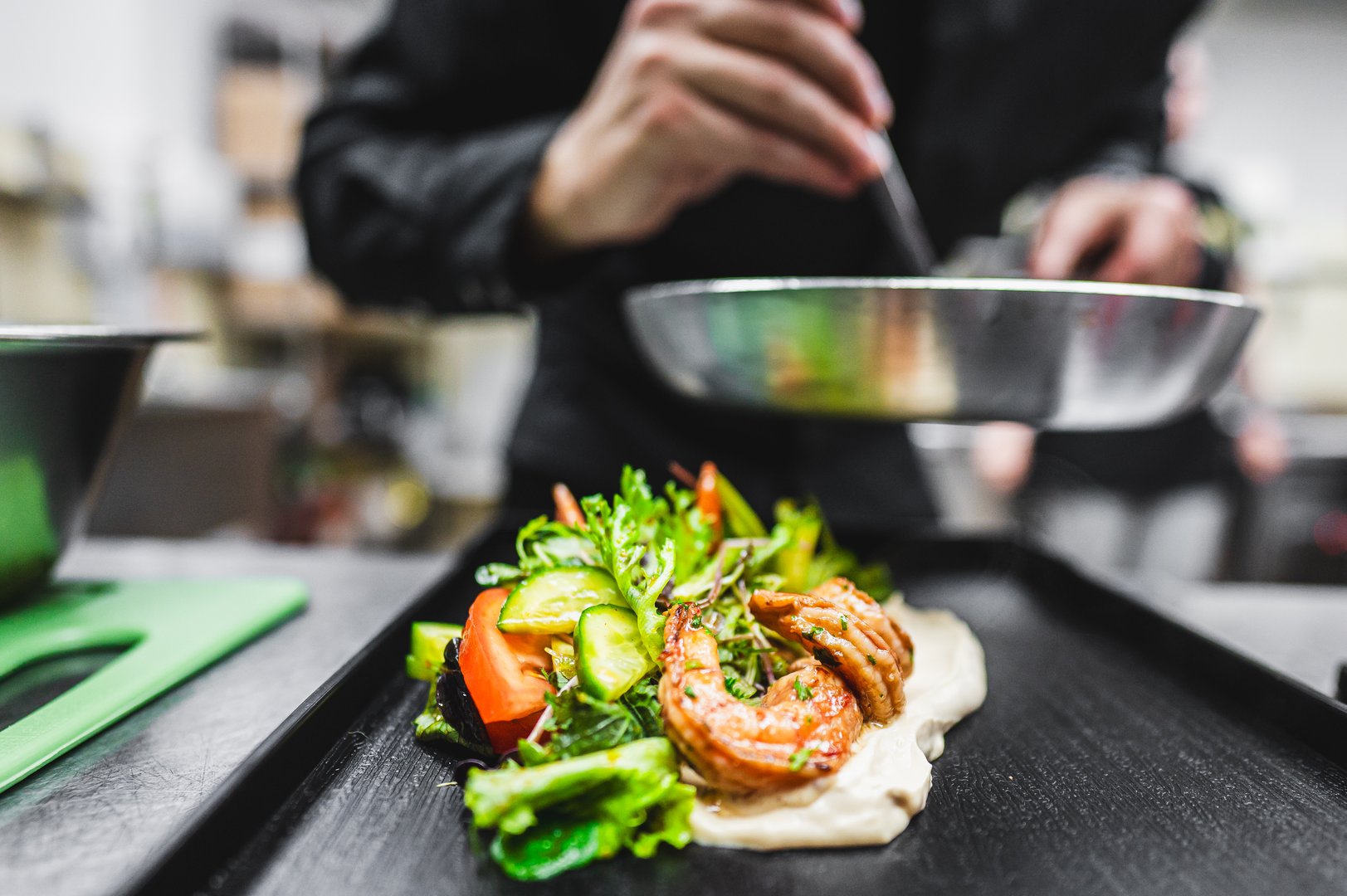 A chef's hands meticulously arranging a fresh salad on a plate, with a blurred kitchen background