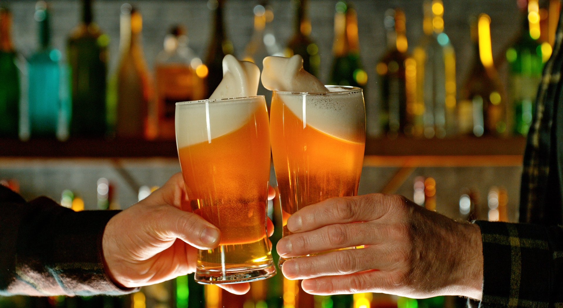 Close-up view of a two glasses of beer in hands. Beer glasses clinking at bar or pub.