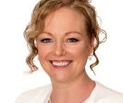 Smiling woman with curly blonde hair wearing a white top against a plain background.