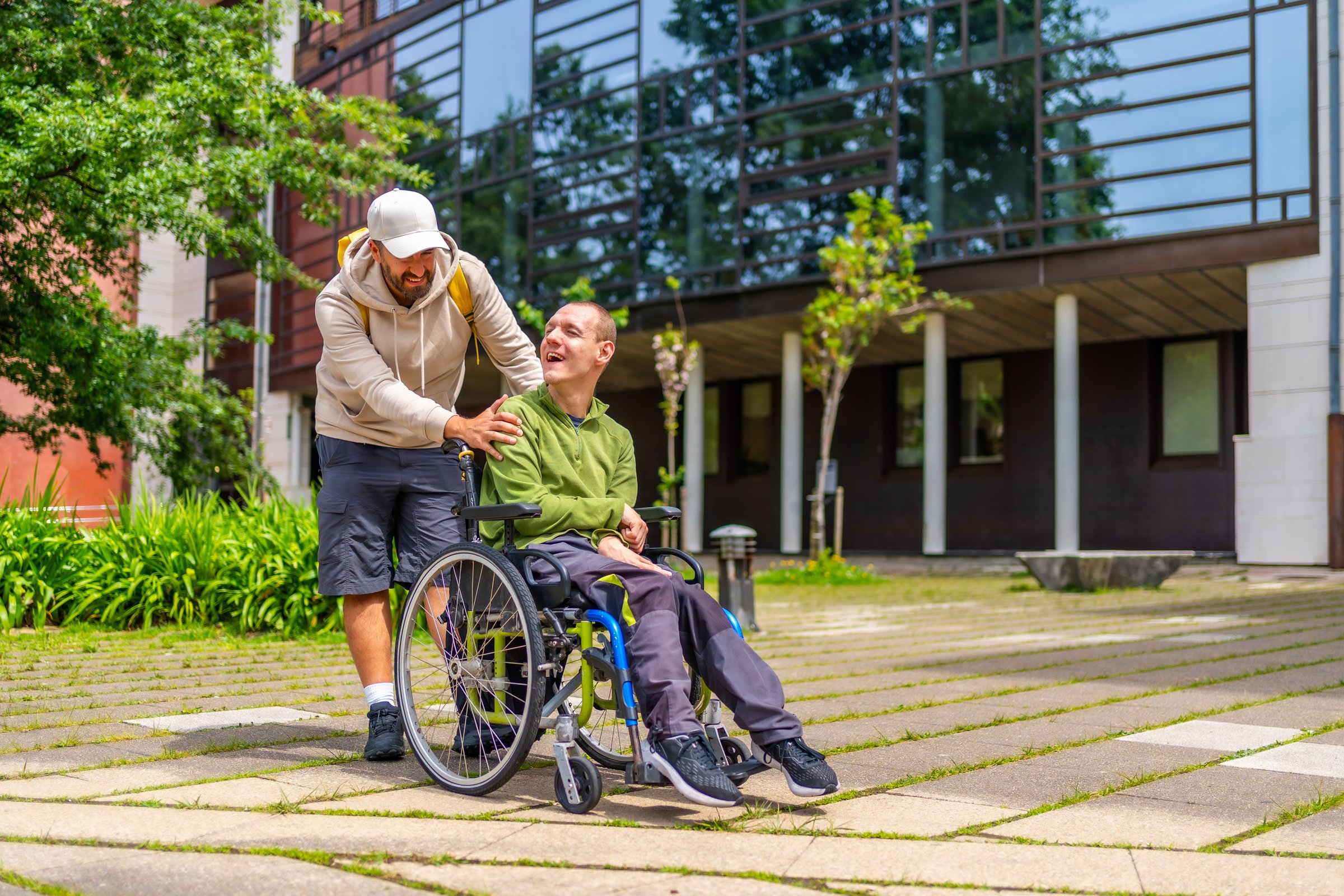 Full length photo of a caucasian adult man with special needs and friend walking along the university campus