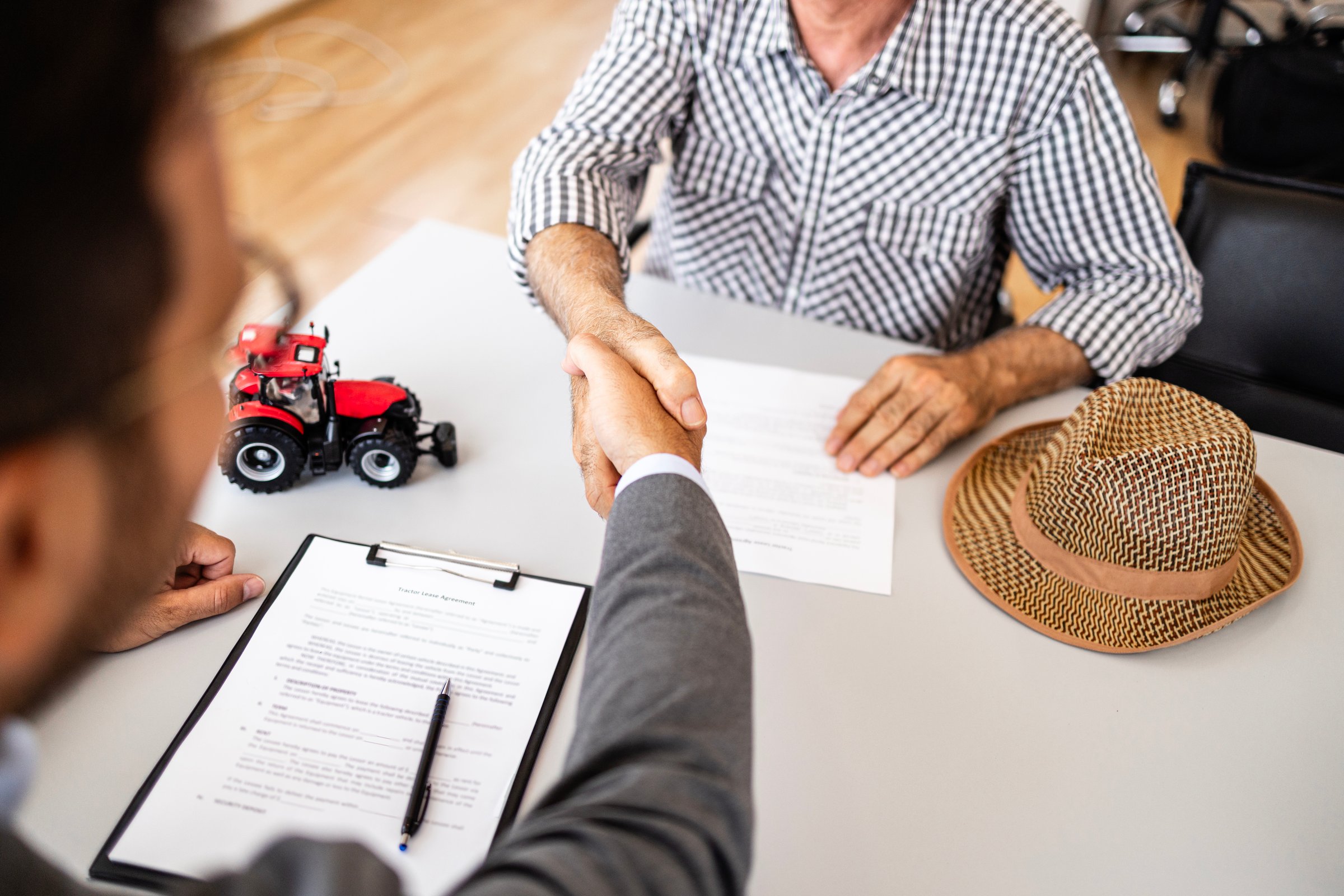 Farmer at tractor dealership signing contract and shaking hands with sales manager after purchasing agricultural machines and equipment