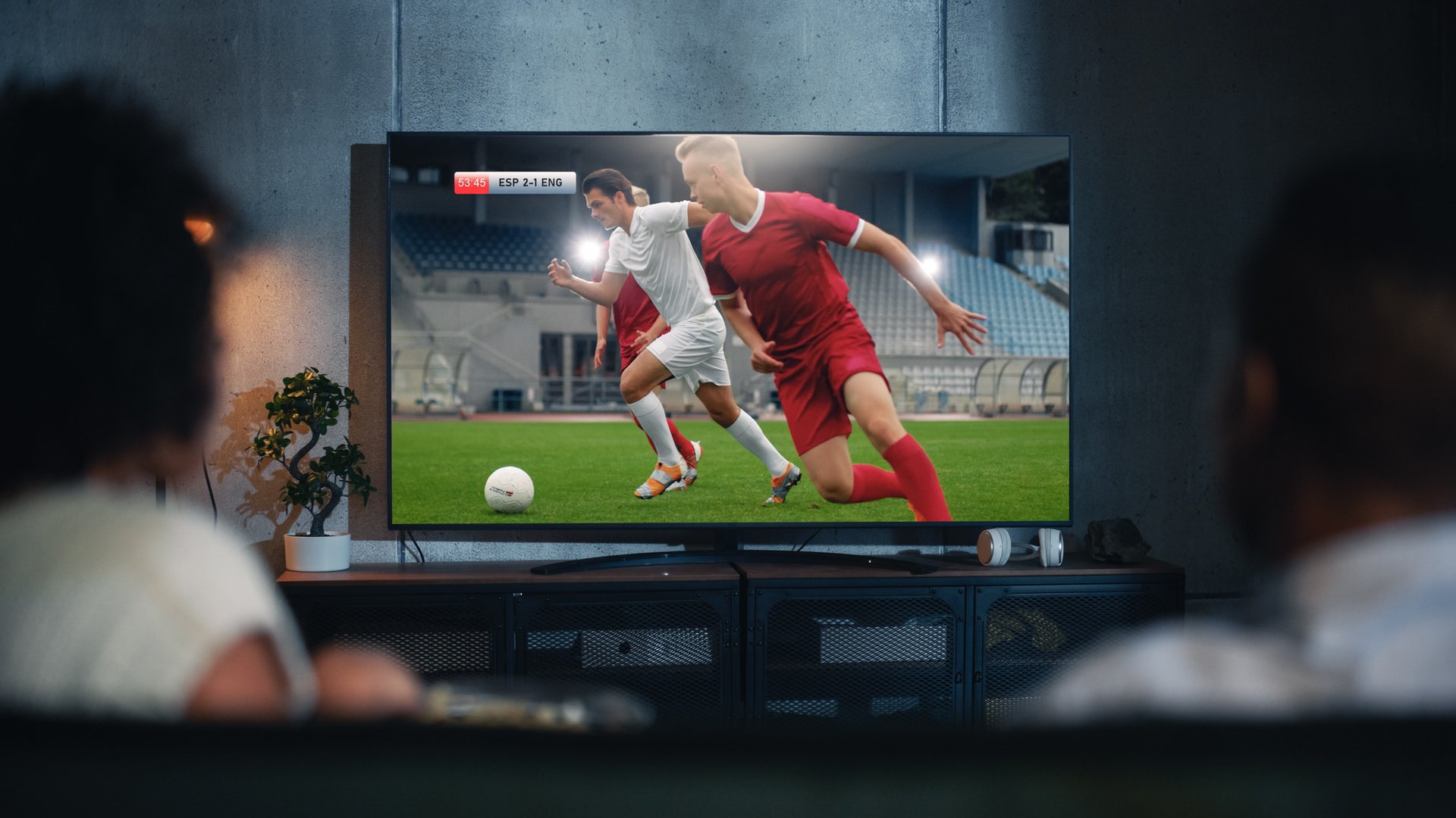 Black Couple Watches Professional Soccer Match on TV, Sitting on a Couch at Home in the Evening. Boyfriend and Girlfriend Football Fans Watch Sports. Back View Out of Focus Close Up Shot at Night.