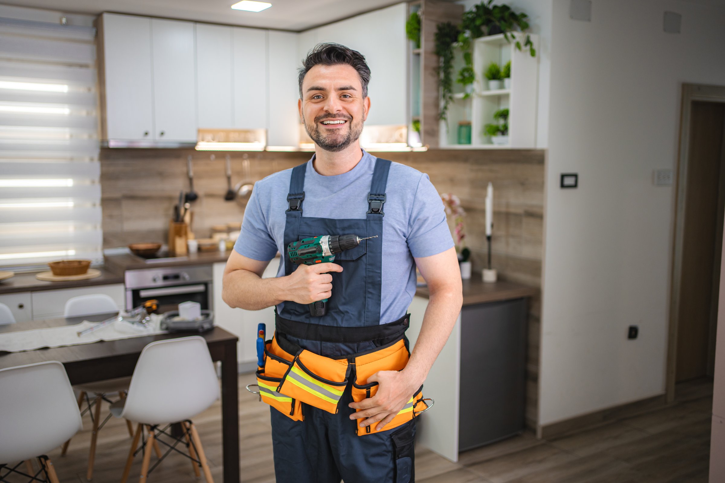 Portrait of a smiling handyman holding a cordless drill in a kitchen
