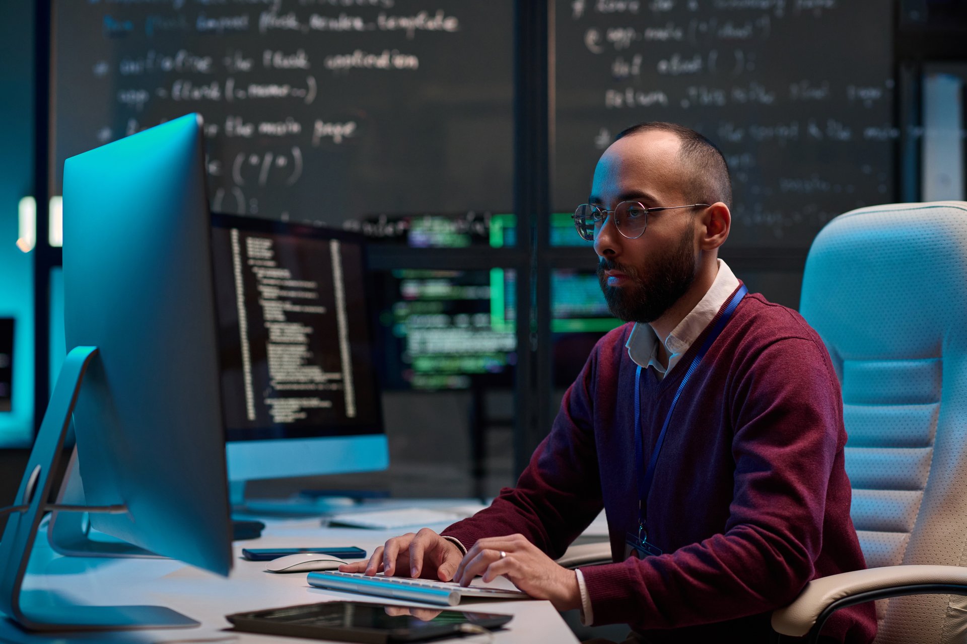 Side view portrait of adult man wearing glasses and writing code using computer in modern cybersecurity department with glass walls copy space