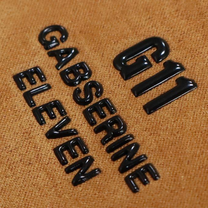 Close-up of black embossed text G11 GABSERINE ELEVEN on a textured brown surface.