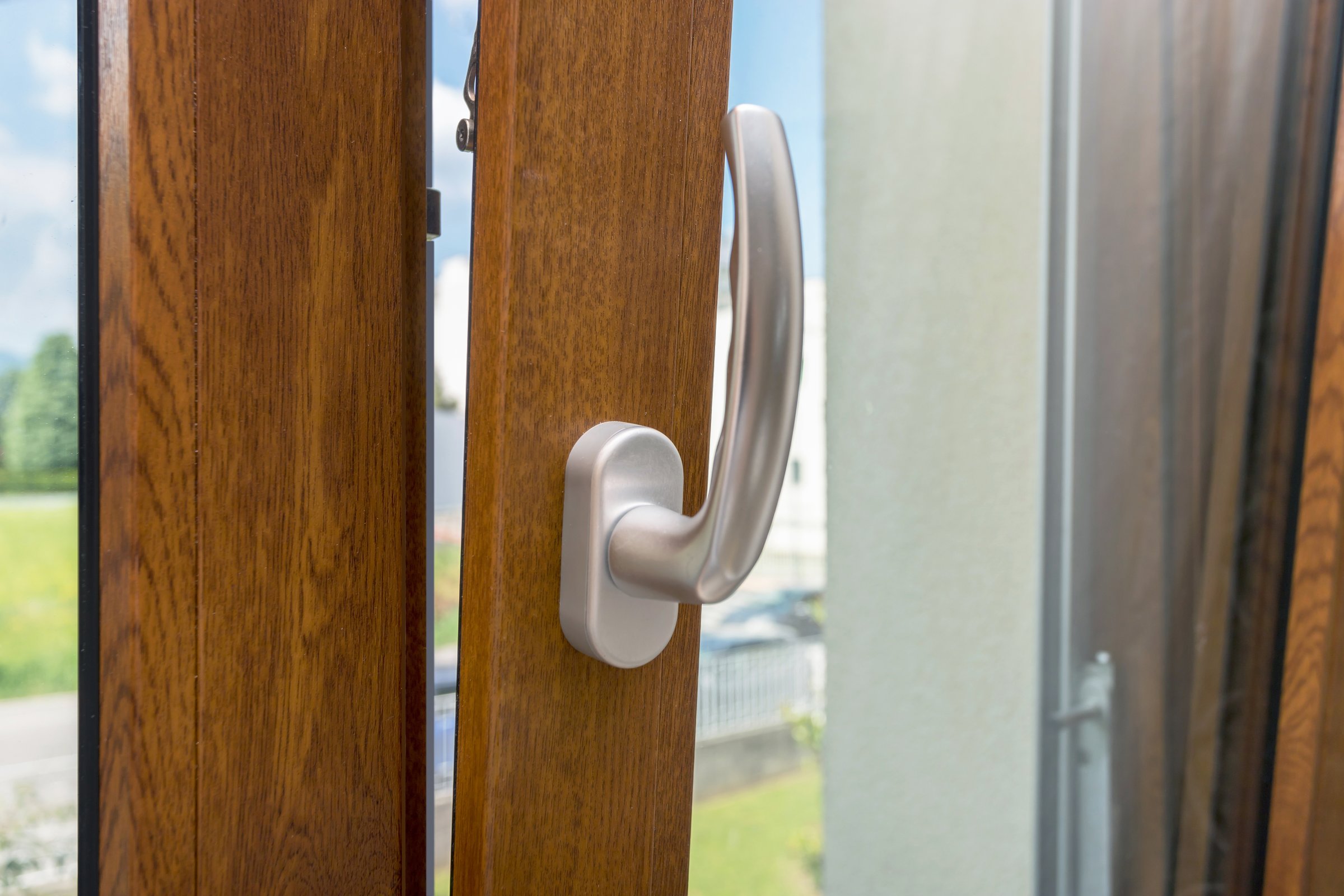 Wooden window open detail. Bottom hung window. Wooden, Metal, PVC door frame closeup view. Stylish chrome handle. Energy efficient and safety profile. Residential garden blurred background.