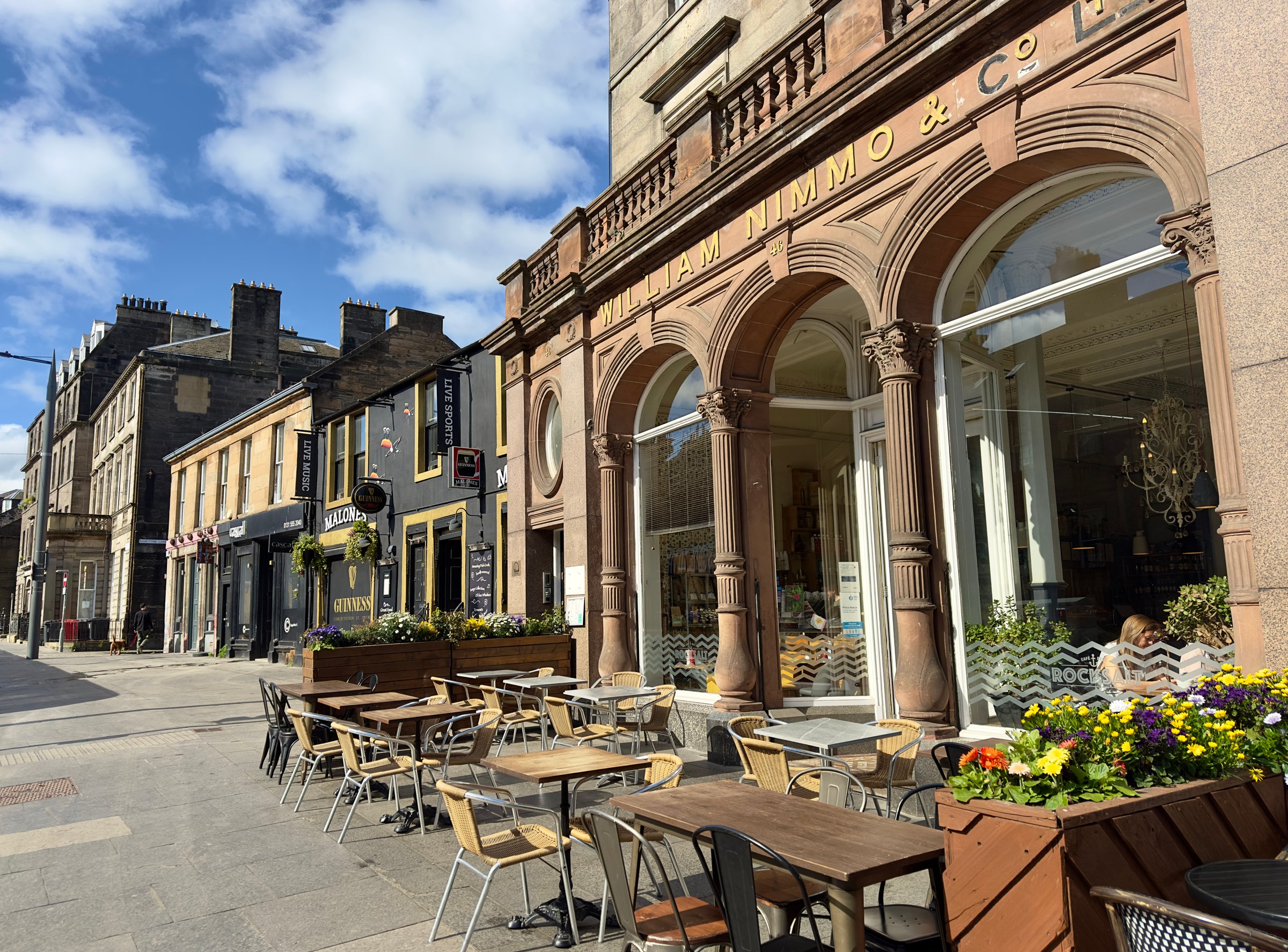 Leith, UK - May 4, 2025: Rock Salt Cafe with outdoor pavement tables on Constitution Street, Leith, Edinburgh, Scotland. Original historic signage on the building for William Nimmo & Co, a printers and stationers business.
