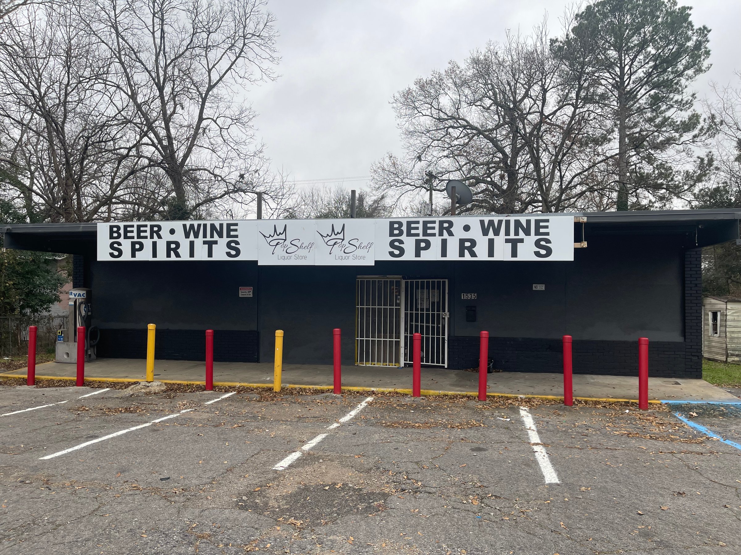 A store with signs for beer, wine, and spirits, featuring red bollards and an empty parking lot.