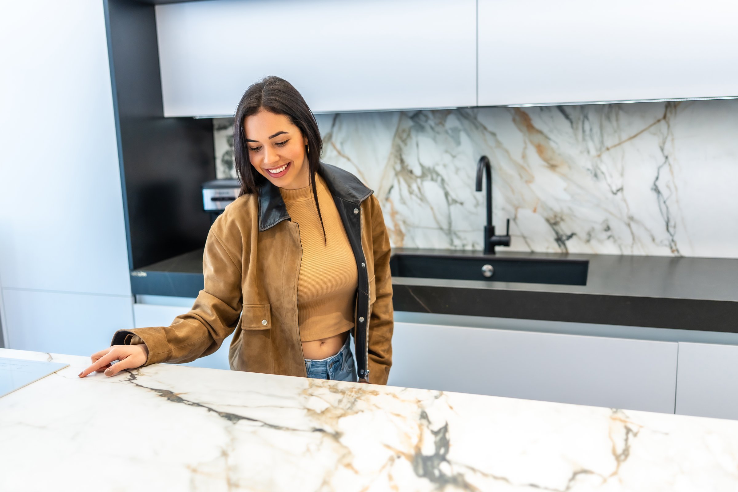 Young woman selecting marble countertop in a modern kitchen showroom, touching the smooth surface and smiling