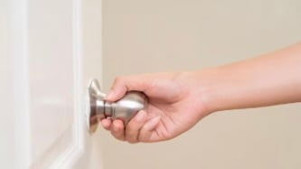 Hand turning a silver door knob on a white door frame