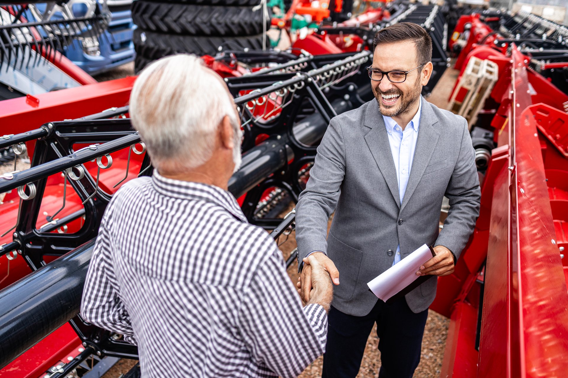 Farmer and tractor salesman shaking hands and discussing about financial plans.