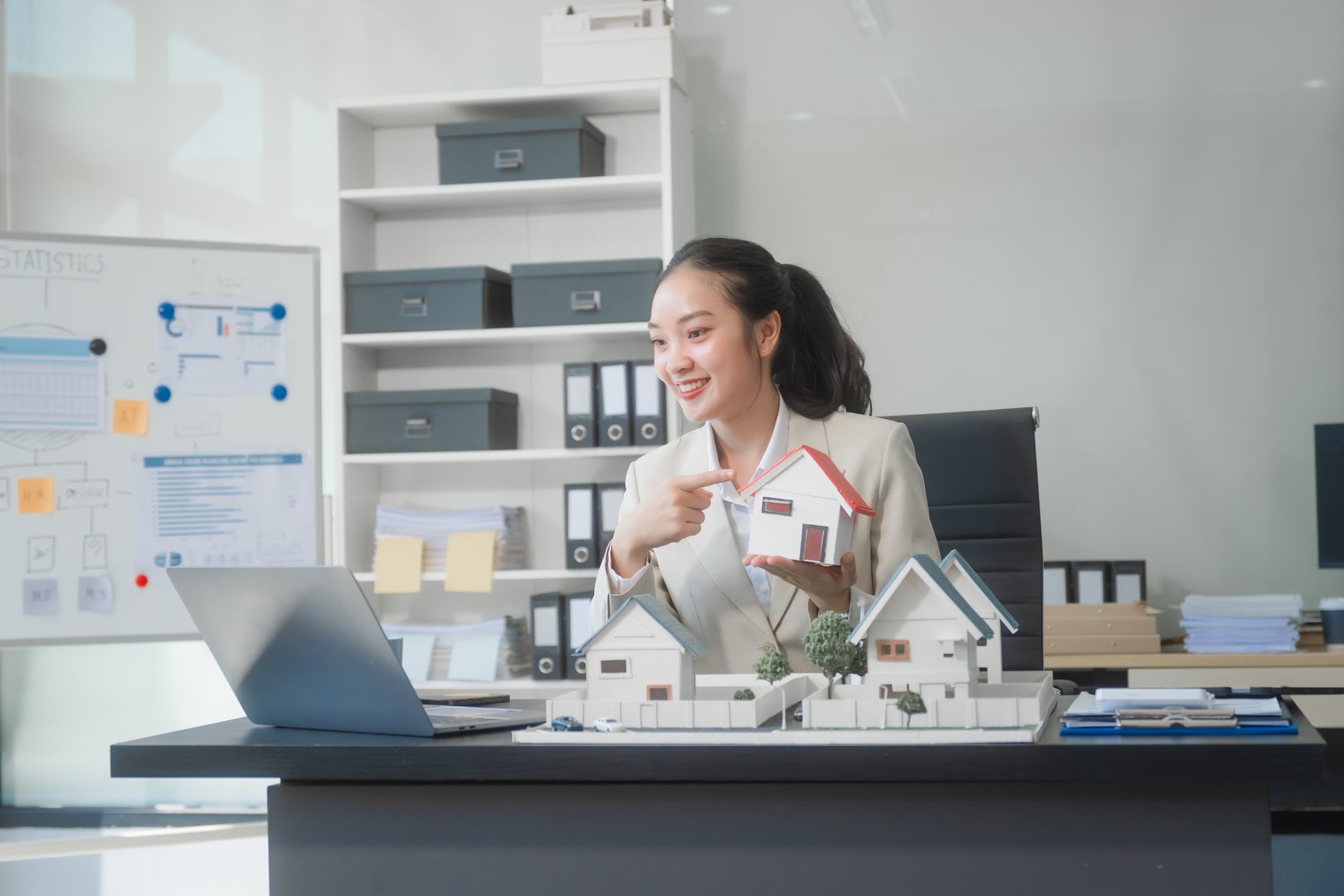 Asian professional woman sits at desk in modern office, reviewing real estate documents and financial plans. confidently, assists with property investments, loans, and contracts, business ventures.