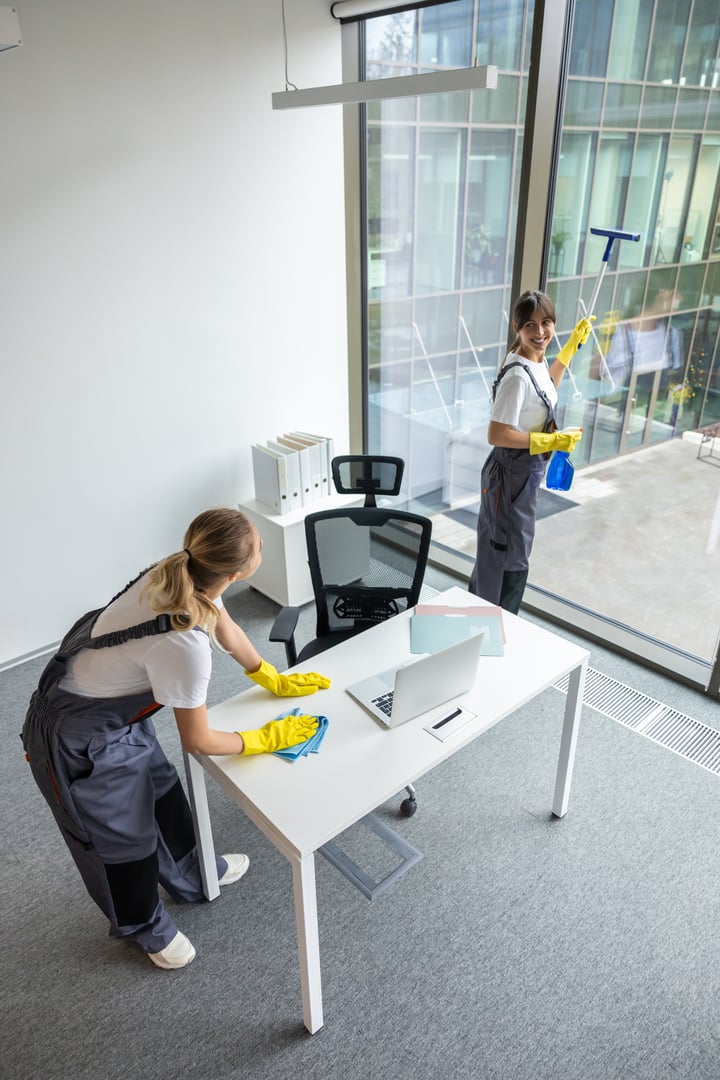 Cleaning in the office. Blonde young woman in yellow gloves cleaning the table in the office