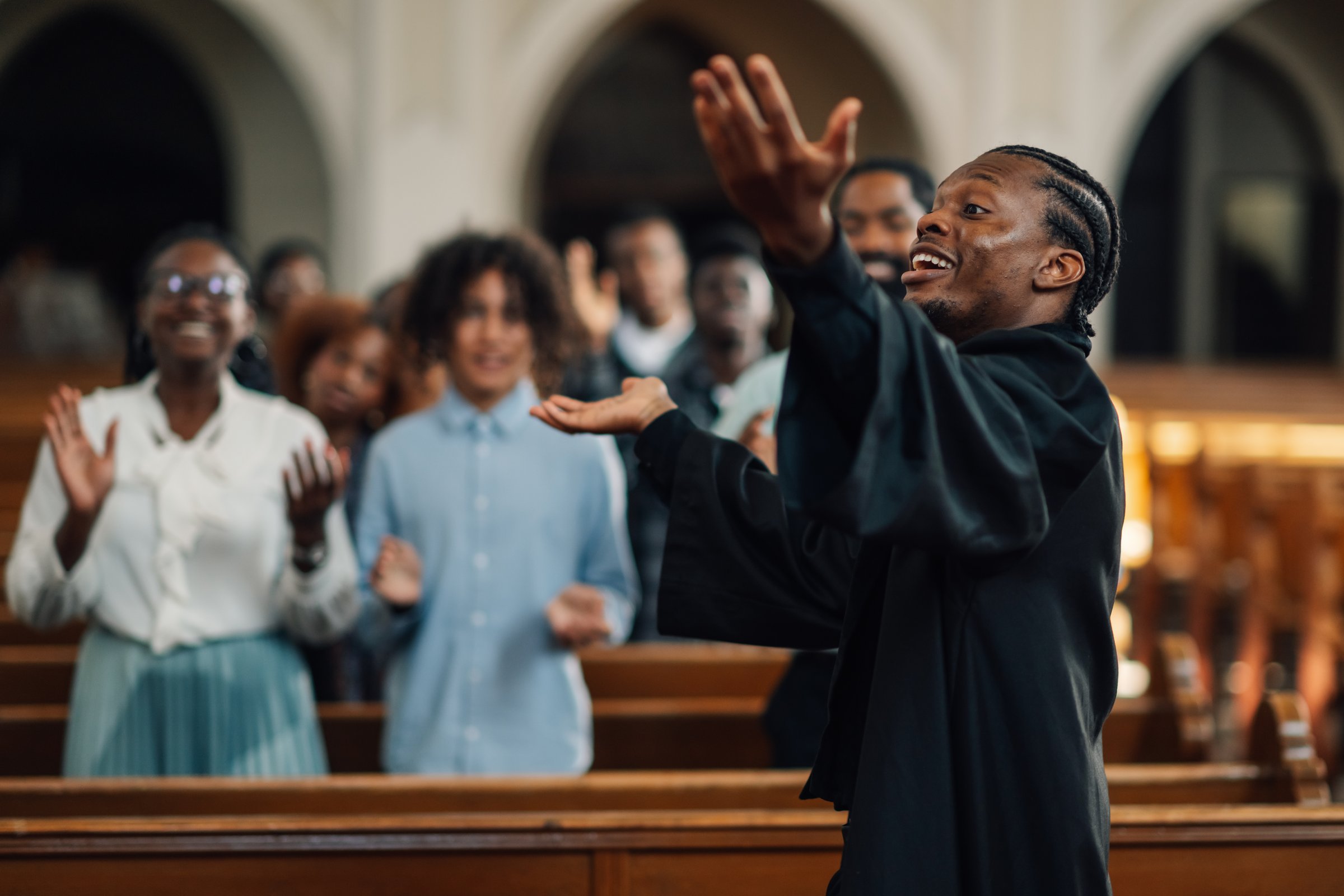 Preacher is delivering a passionate sermon, his hands raised in the air as he speaks to the diverse congregation gathered in the church pews