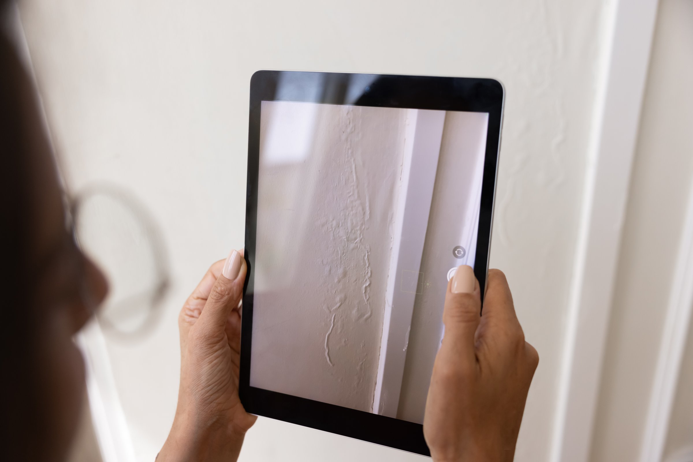 Woman taking pictures of renovation defects of wallpapers, recording damaged wall decoration in apartment, using digital tablet, preparing claim for insurance agency, making inspection of rental